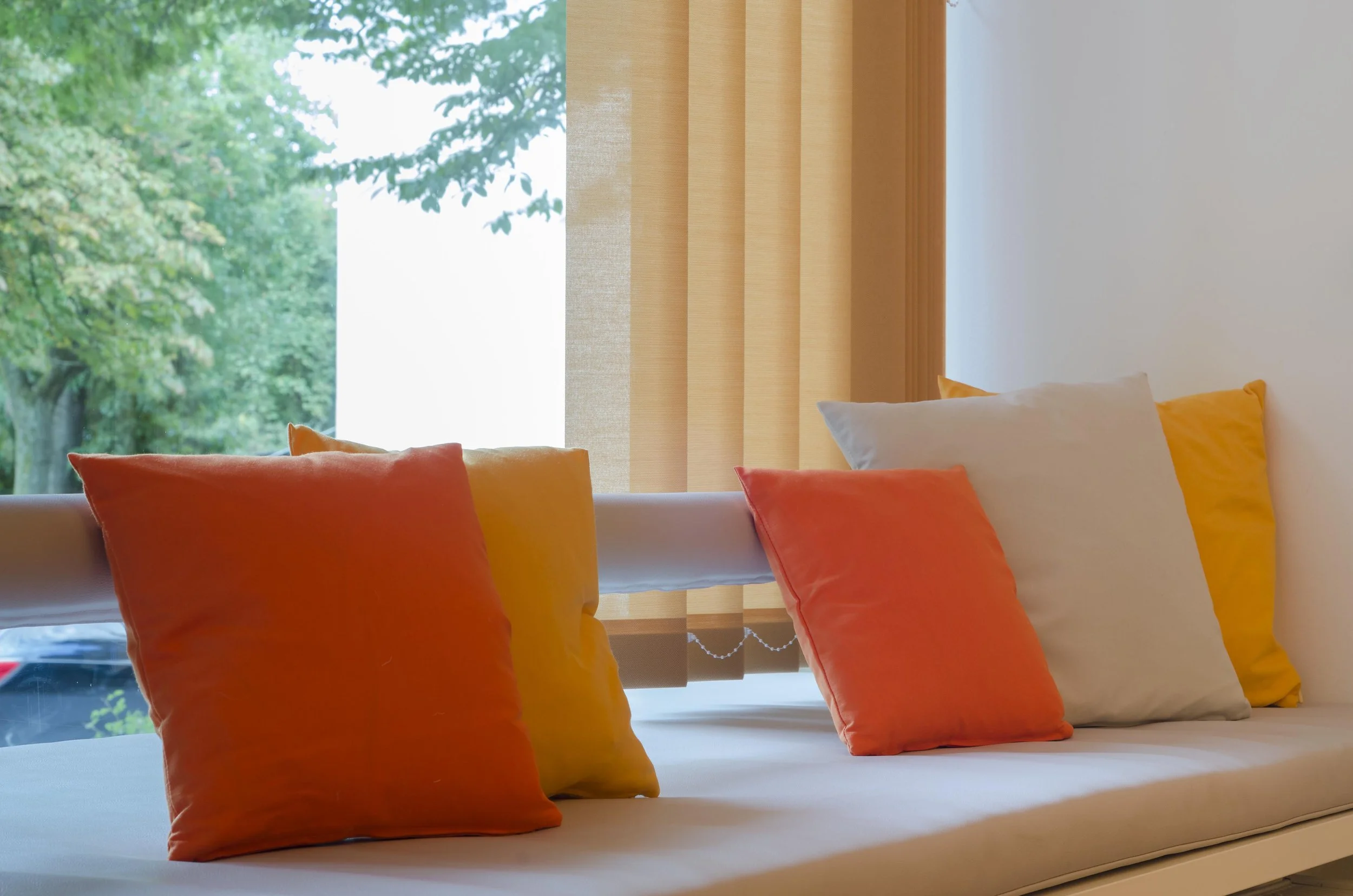 Sofa mit bunten Kissen vor einem Fenster mit Blick auf Bäume im Grünen