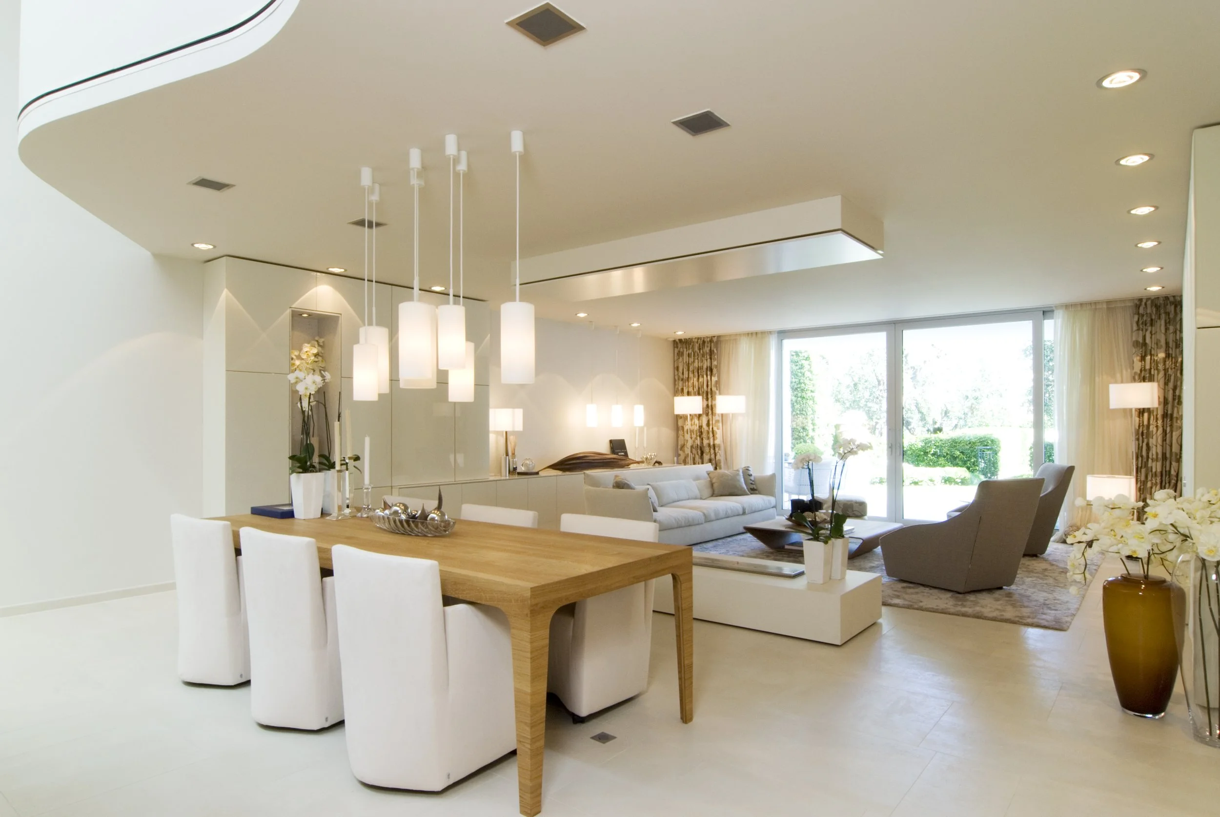 Modernes, helles Wohnzimmer mit großen Fenstern, eleganter Essbereich mit HolzTisch und weißen Stühlen, bequemen Sofas und dekorativen Elementen, viel natürlichem Licht.