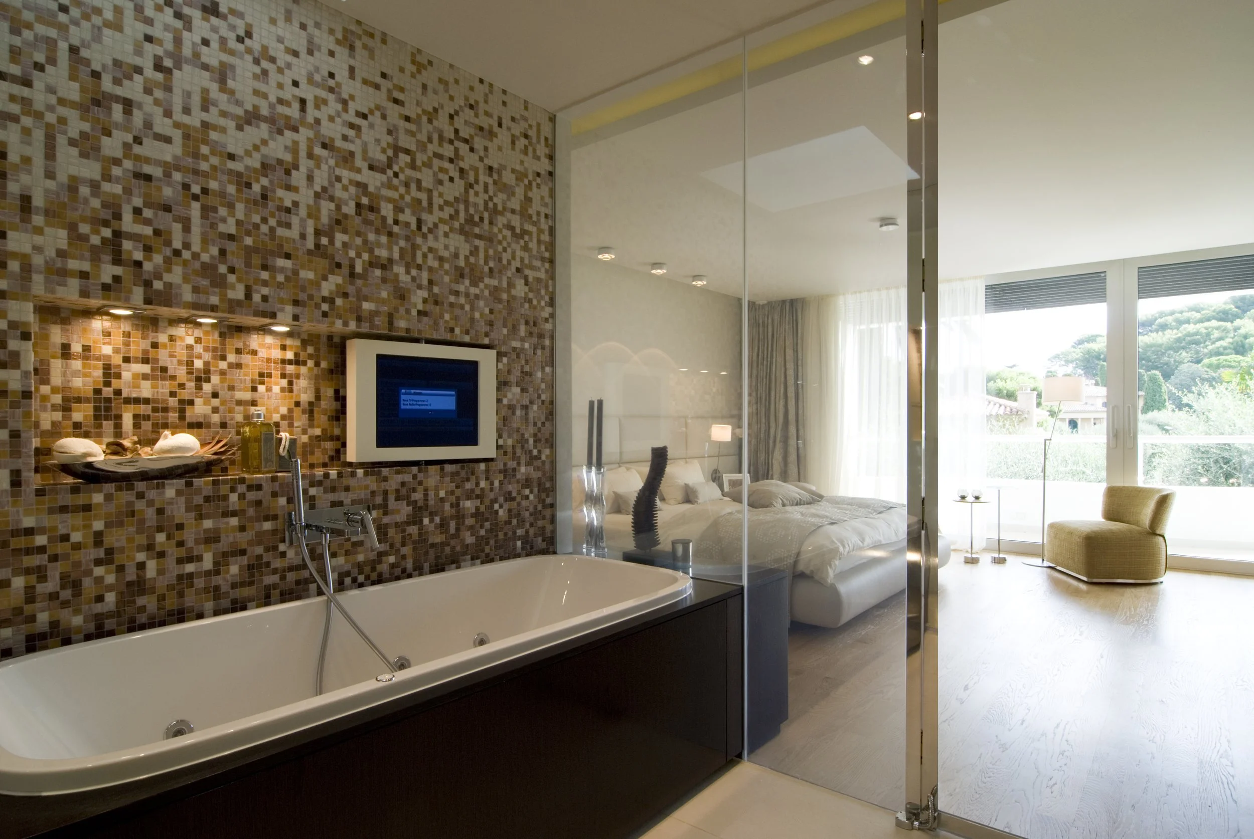 Ein moderates Hotelzimmer mit Bad, Badewanne, Schlafzimmer und Balkon, große Fenster mit Blick auf die Natur.