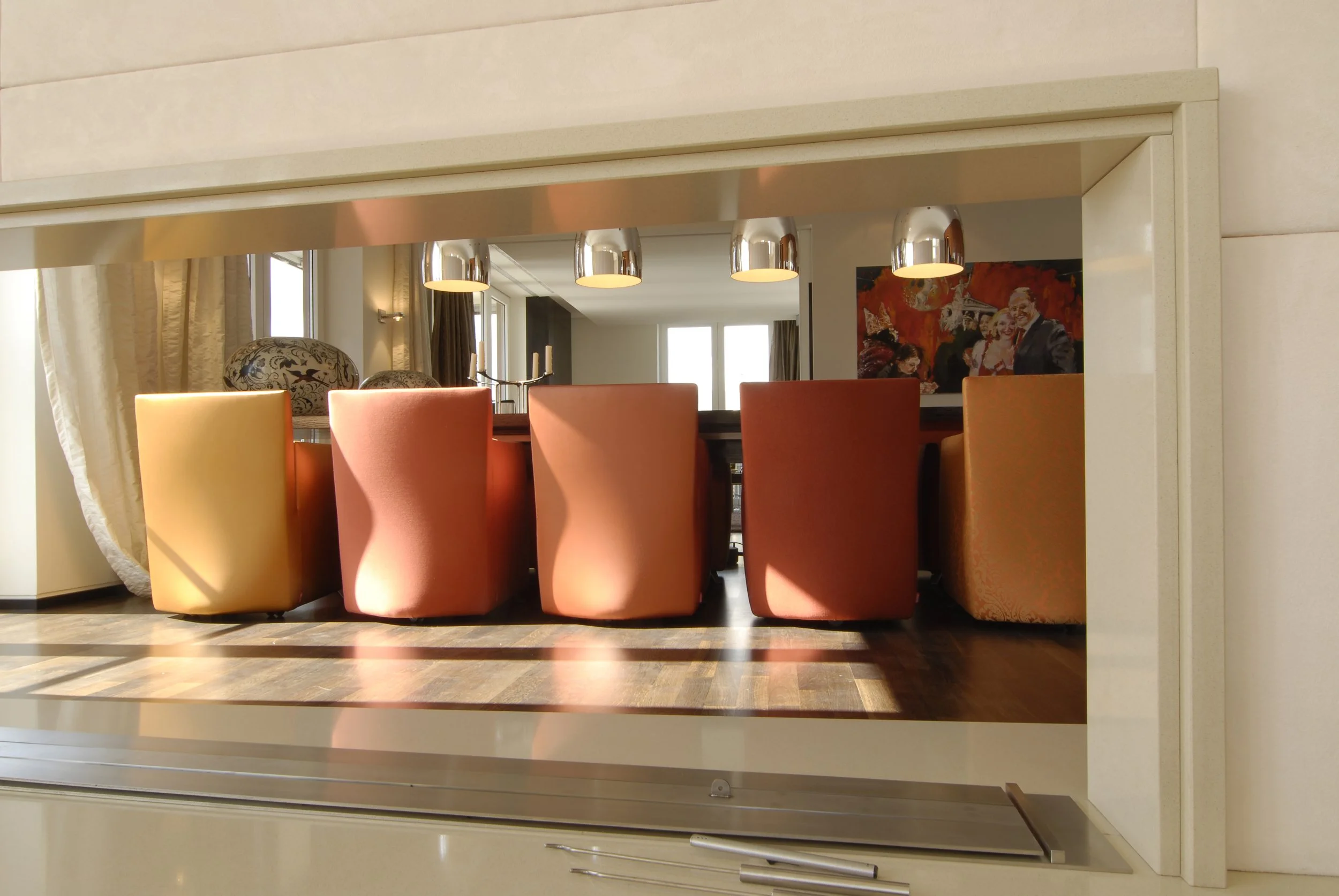 Blick auf einen Essbereich mit bunten Sessel, modernen Lampen und einer Wand mit Gemälde in einem hellen, eleganten Zimmer.