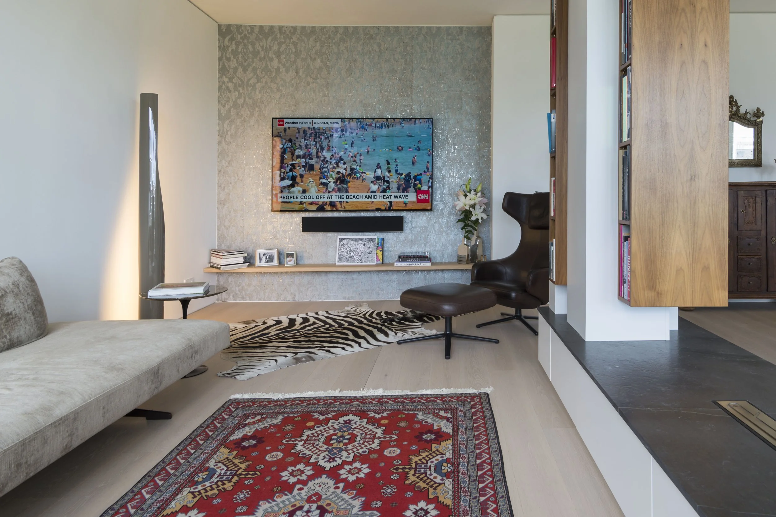 Moderne Wohnzimmereinrichtung mit Fernseher, Sessel, Zebra- und Rug-Dekoration, Bücherregal, Blumen und dekorative Elemente.