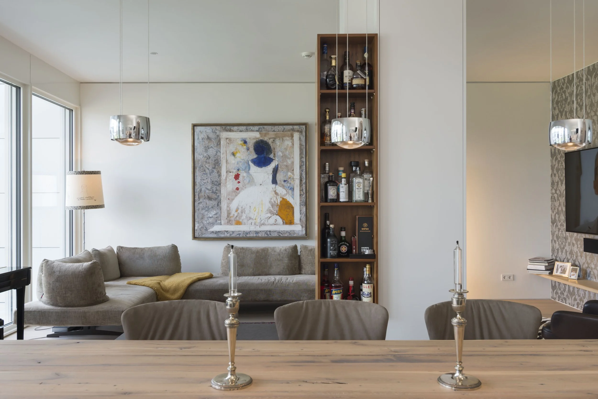 Moderner Wohnzimmerbereich mit grauer Couch, Wandkunst, offener Bar mit Flaschen, Tisch mit Kerzen, Sofa, Fernseher und Bücher