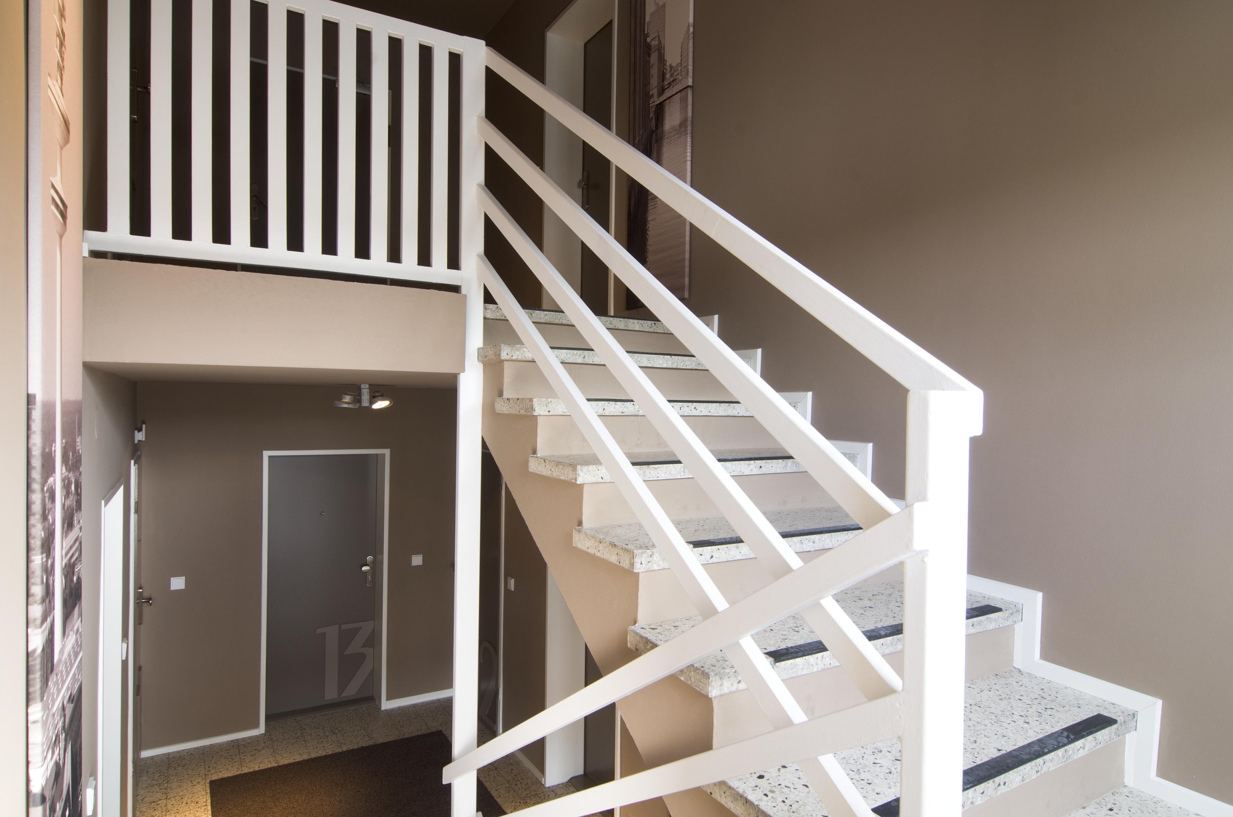 Innenaufnahme eines Mehrfamilienhauses mit Treppe, grauer Tür und beige Wänden.