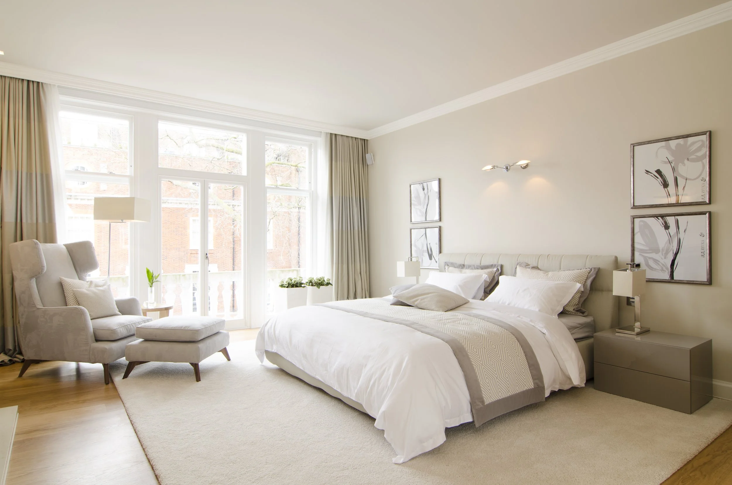 Ein modern eingerichtetes Schlafzimmer mit großem Bett, Nachttischen, Sesseln und großem Fenster mit Vorhängen.