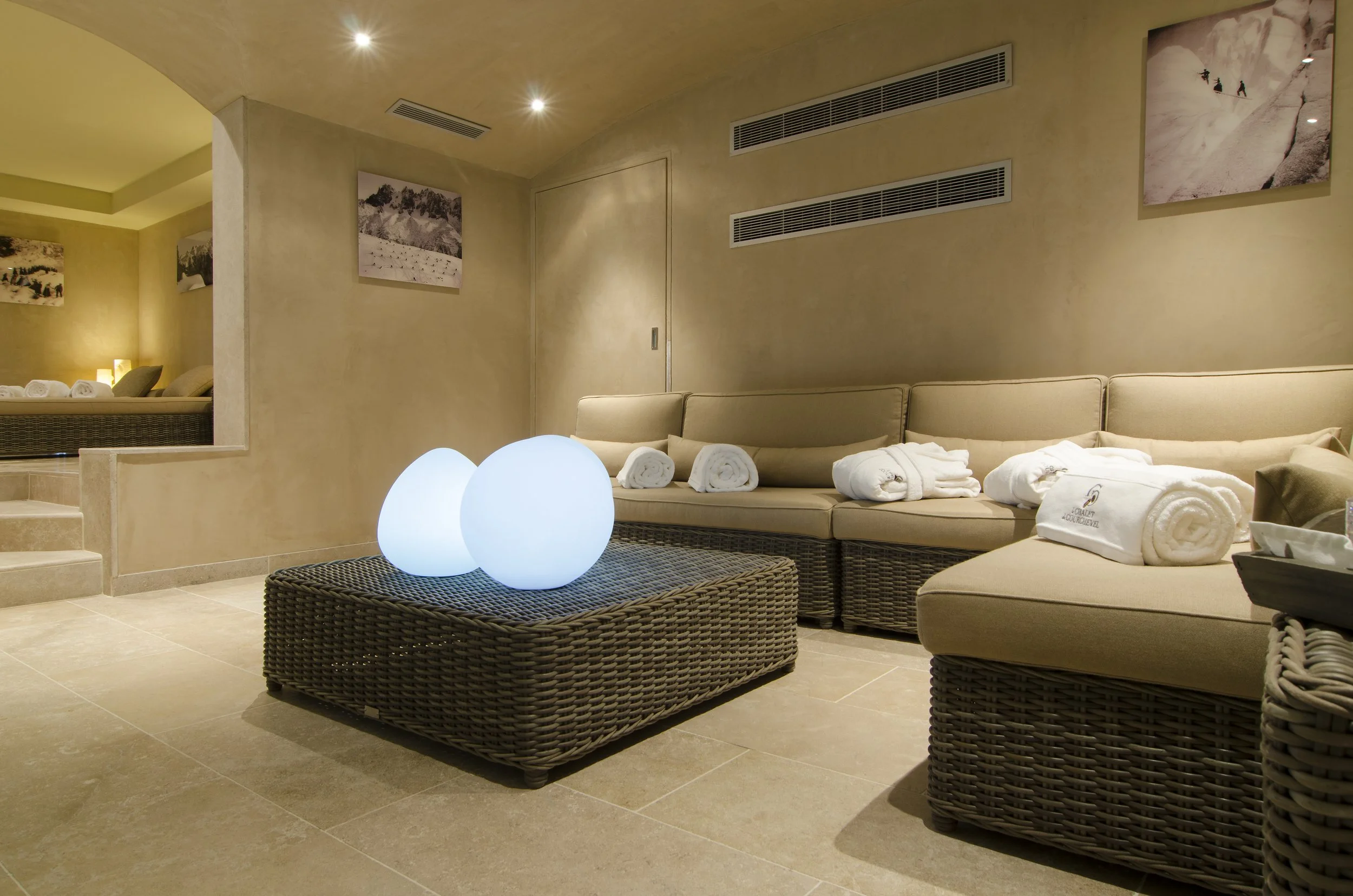 Heller Spa-Bereich mit rattan Möbeln, beleuchteten Dekorationsobjekten, weißen Handtüchern und Wandbildern.