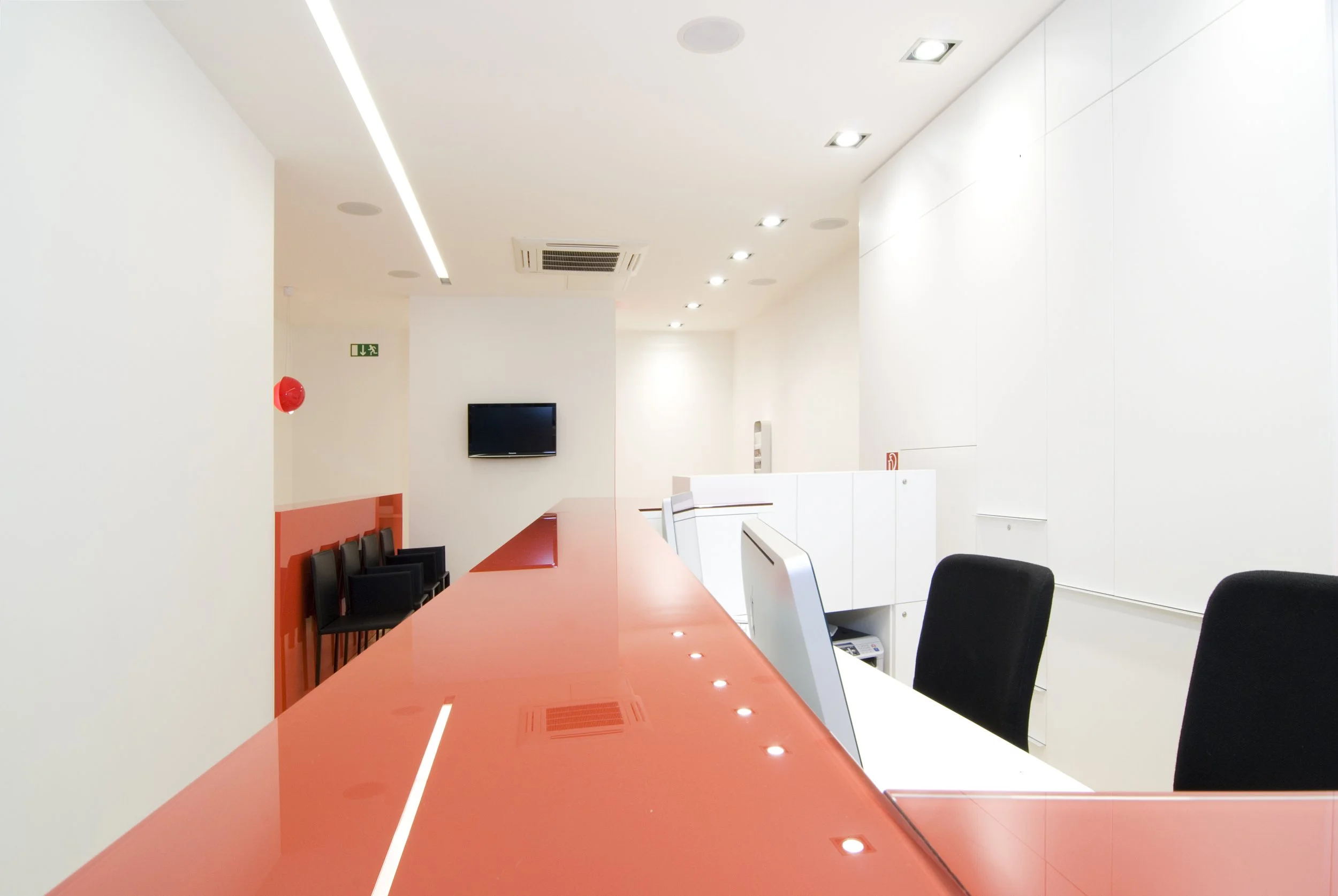 Leerer Empfangstresen in einem modernen, weißen Büro mit schwarzem Sitzmobiliar, einem kleinen Fernseher an der Wand, leuchtend weißen Wänden und Deckenbeleuchtung.