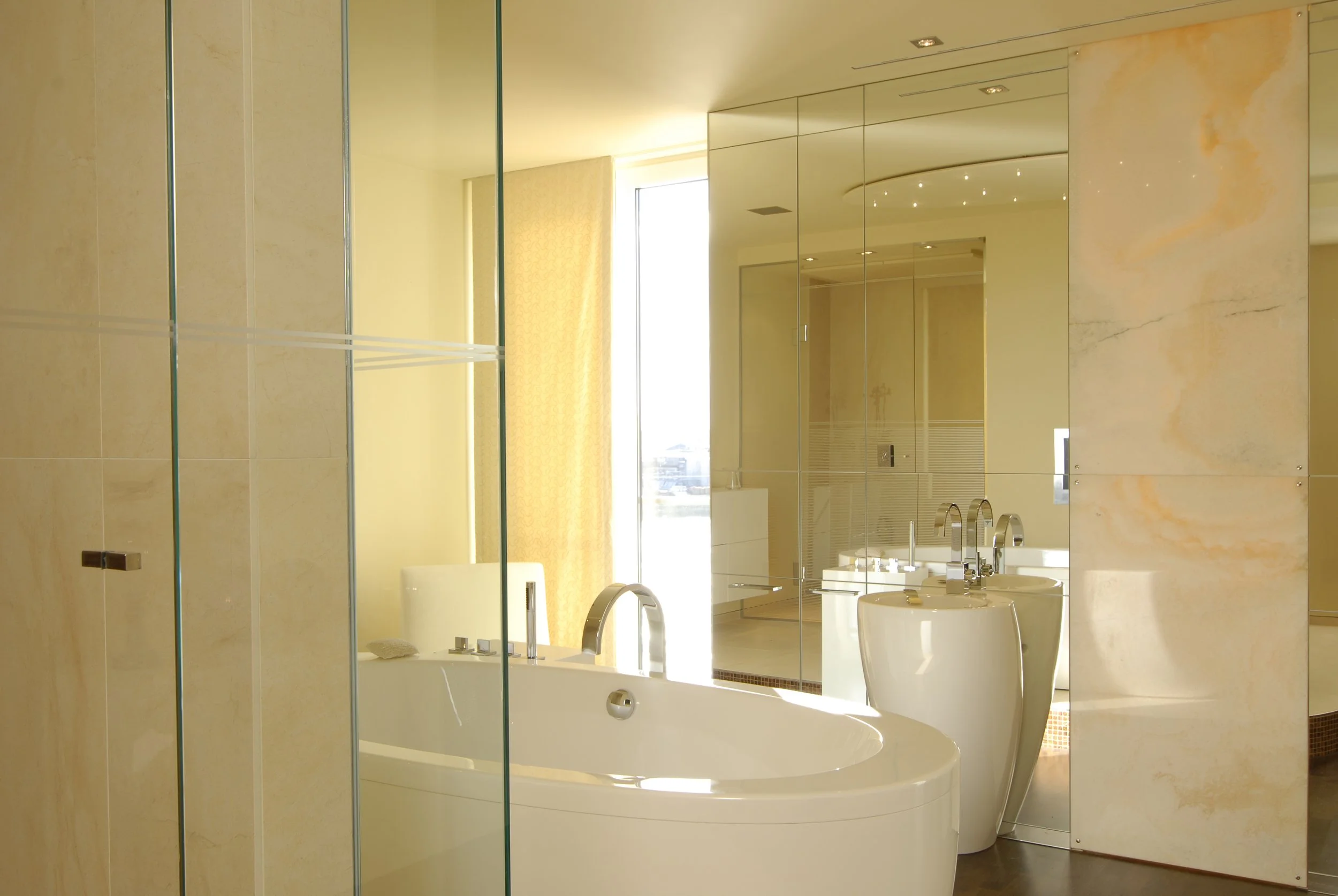 Moderner, luxuriöser Badezimmerbereich mit Badewanne, Doppelwaschbecken und großem Spiegel, Sonnenlicht strömt durch große Fenster.