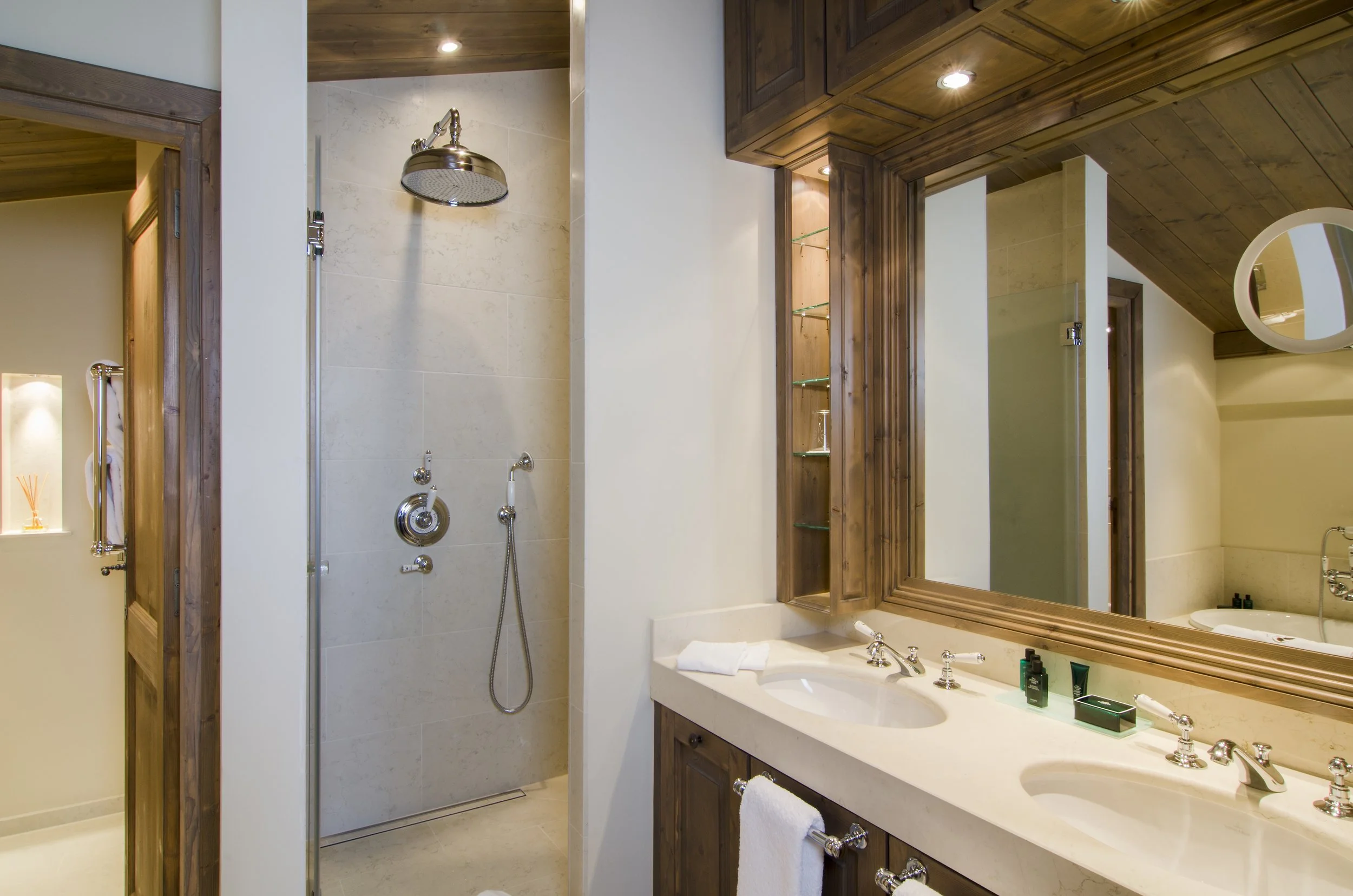 Badezimmer mit Holzmöbeln, Doppelwaschbecken, großem Spiegel, Dusche mit Regendusche, Keramikfliesen und dekorativen Holzelementen.