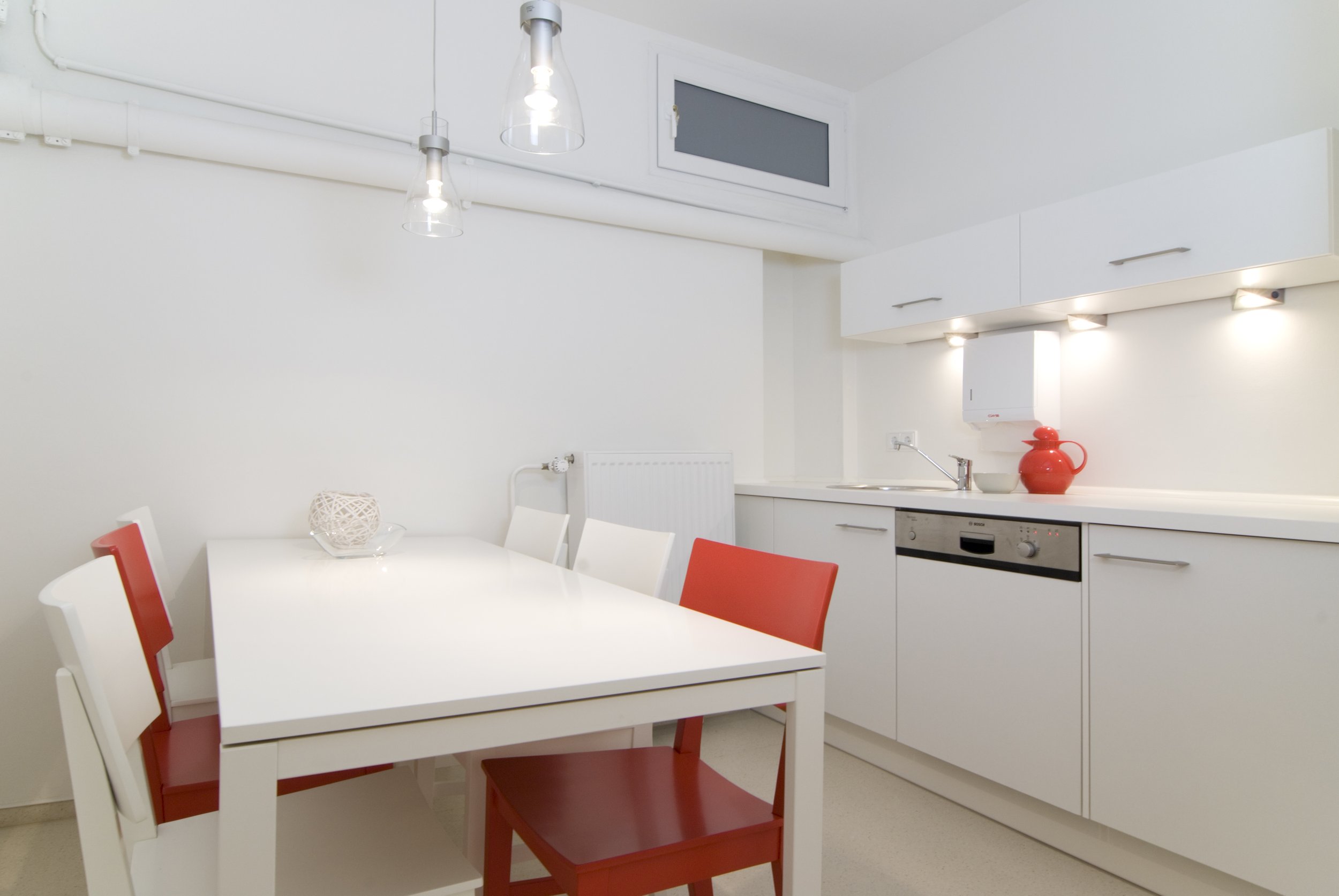 Moderne, weiße Küche mit rotem Akzent, Esstisch und Stühlen