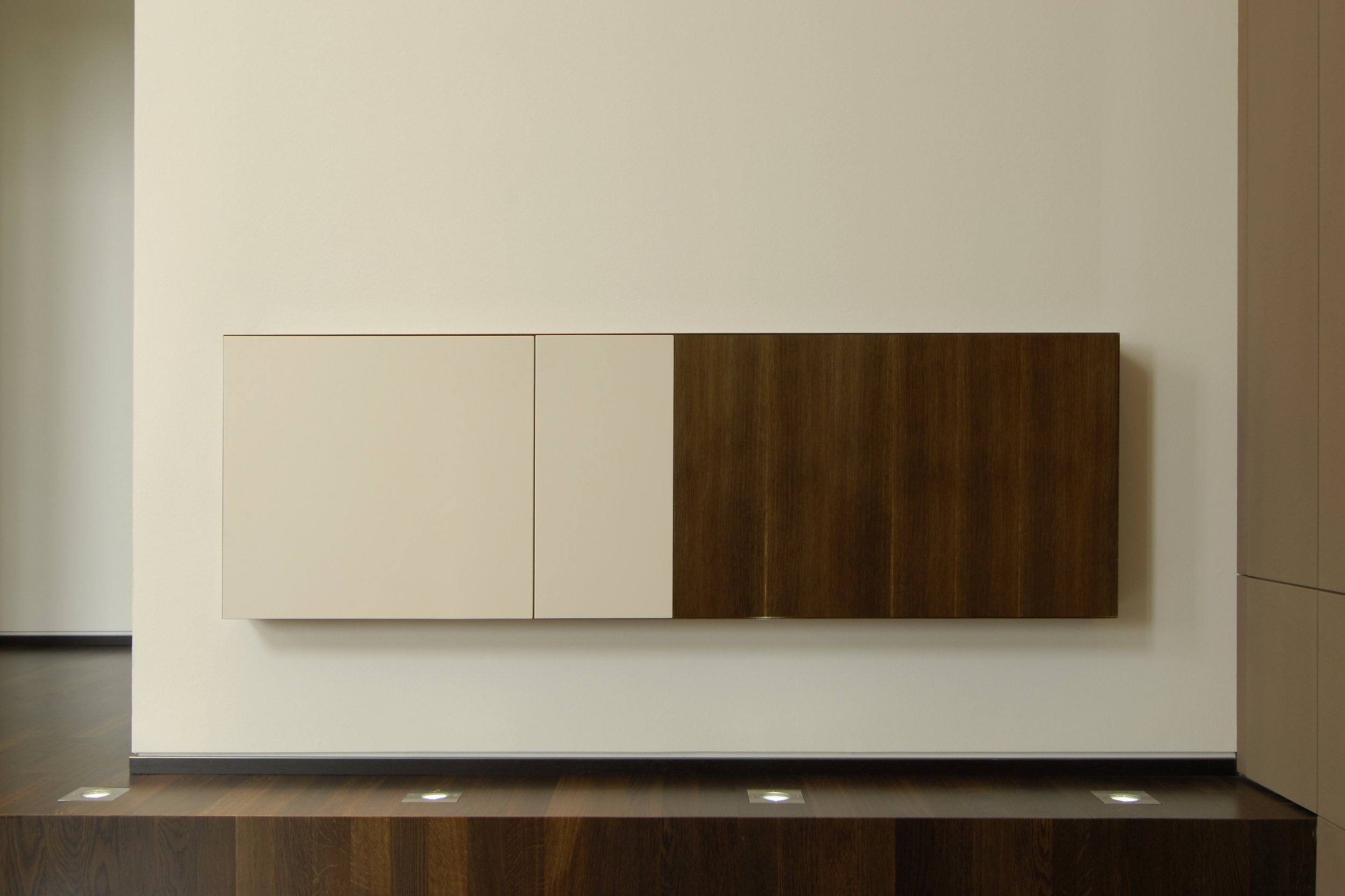 Moderne Wand mit weißen und braunen Holzpaneelen an einer weißen Wand, beleuchtet von eingebauten Deckenleuchten.