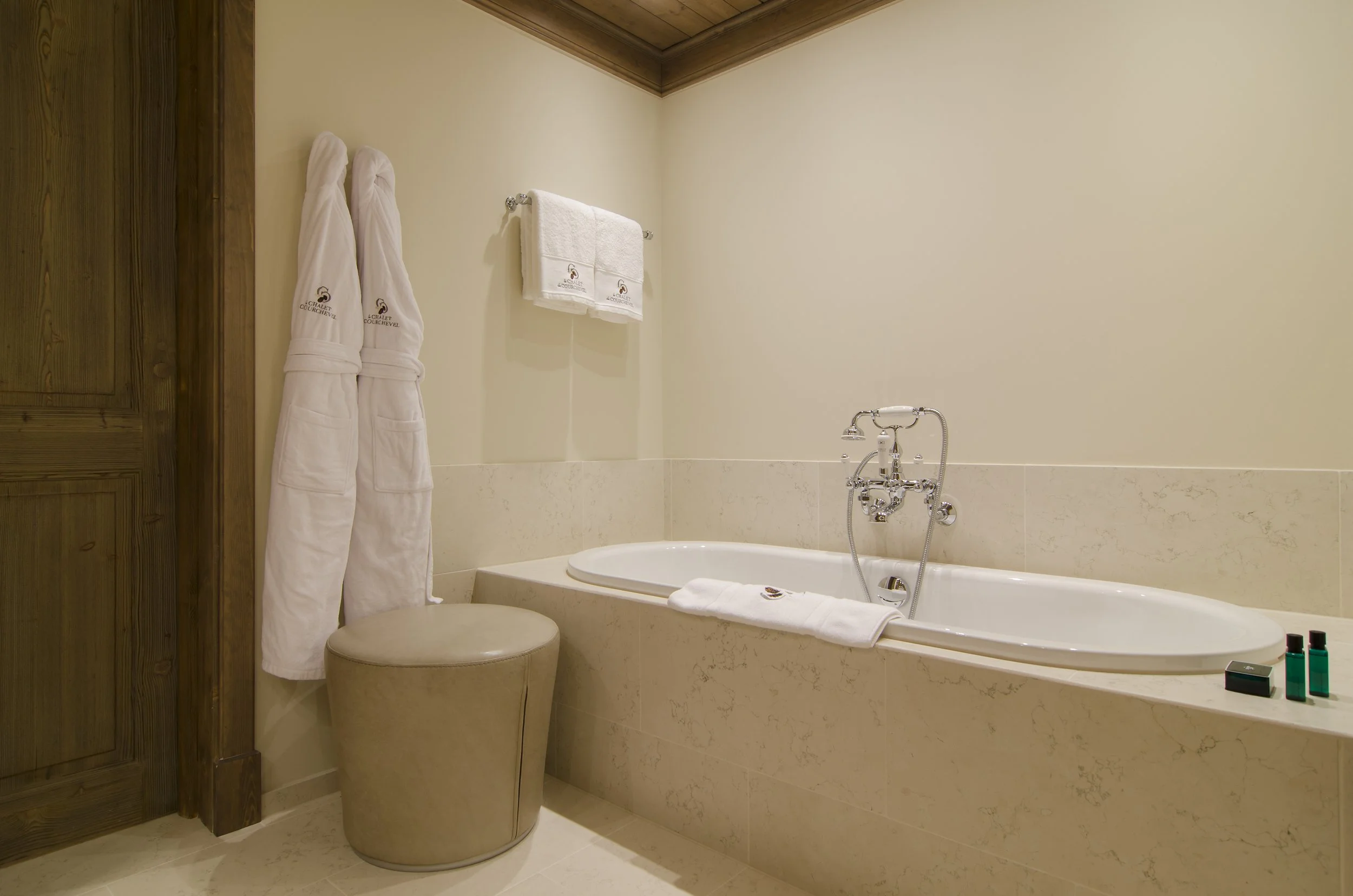 Ein Badezimmer mit Badewanne, weißen Handtüchern und Bademänteln, Holzdecke und neutralen Wandfarben.