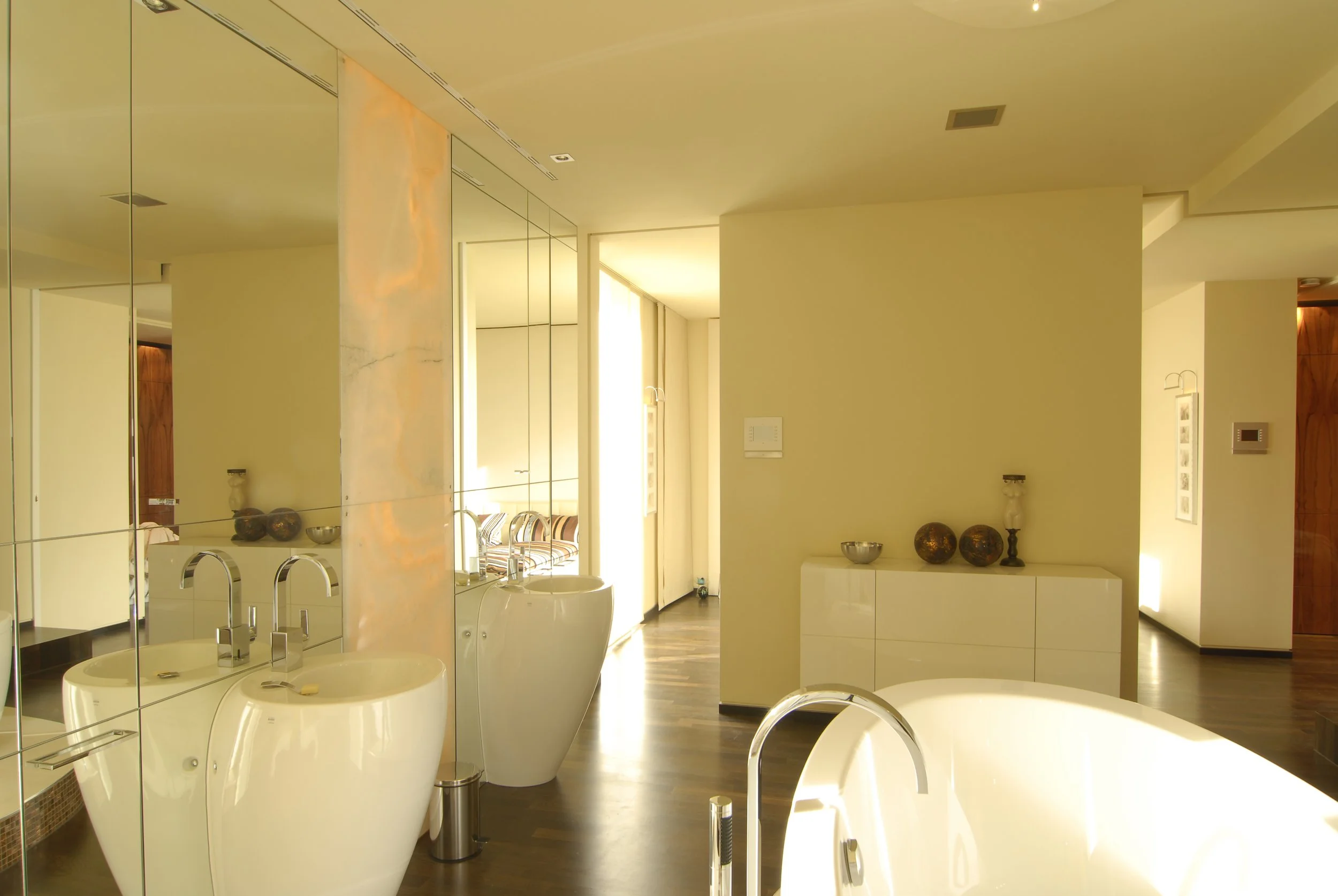 Moderne Badezimmer mit Badewanne, Doppelwaschbecken, Spiegel, hellem Licht und dekorativen Gegenständen auf Sideboard.