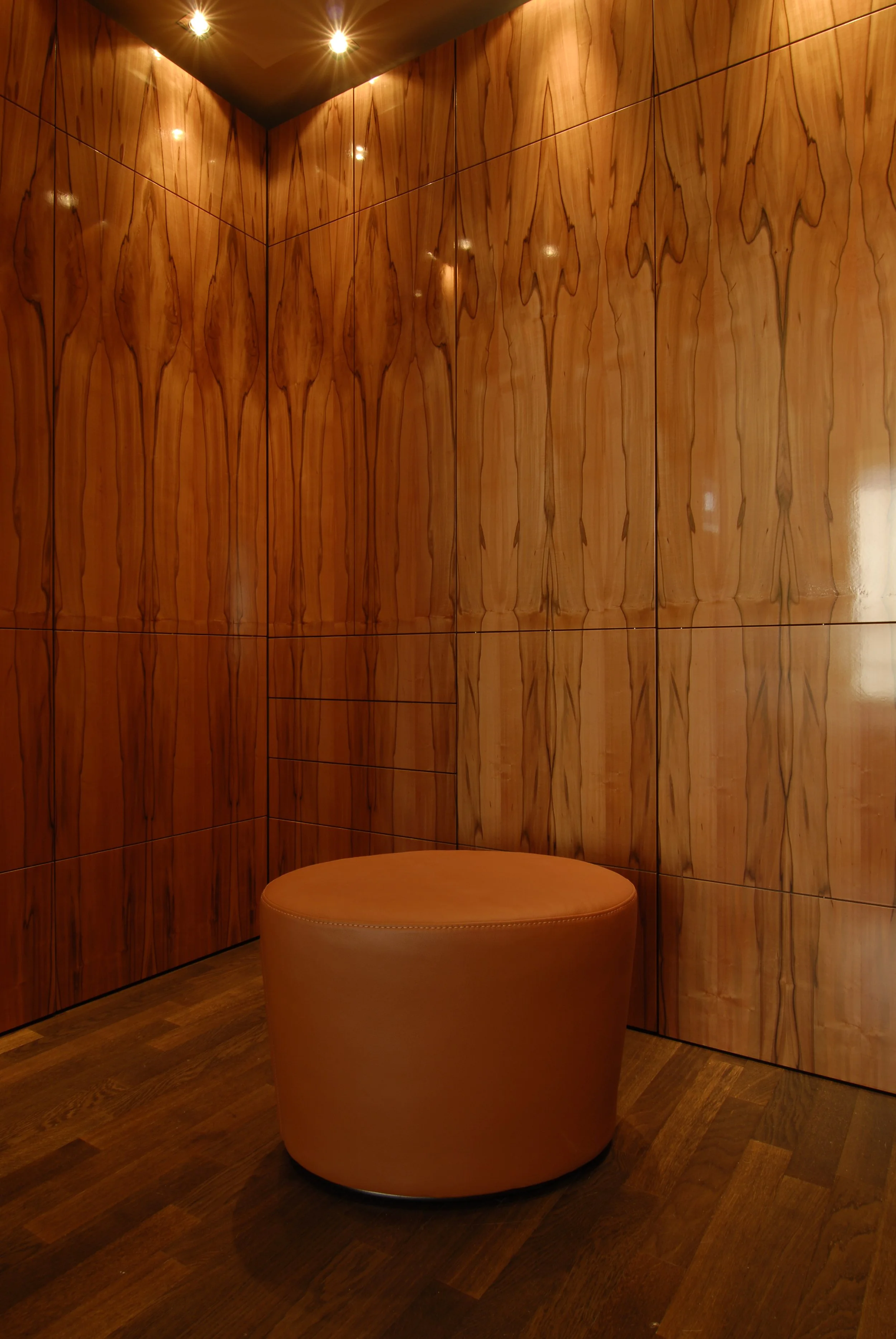 Ein Raum mit Holzverkleidung an den Wänden und einer runden, gepolsterten orangefarbenen Sitzgelegenheit. Die Decke hat mehrere kleine, eingebettete Lichter.
