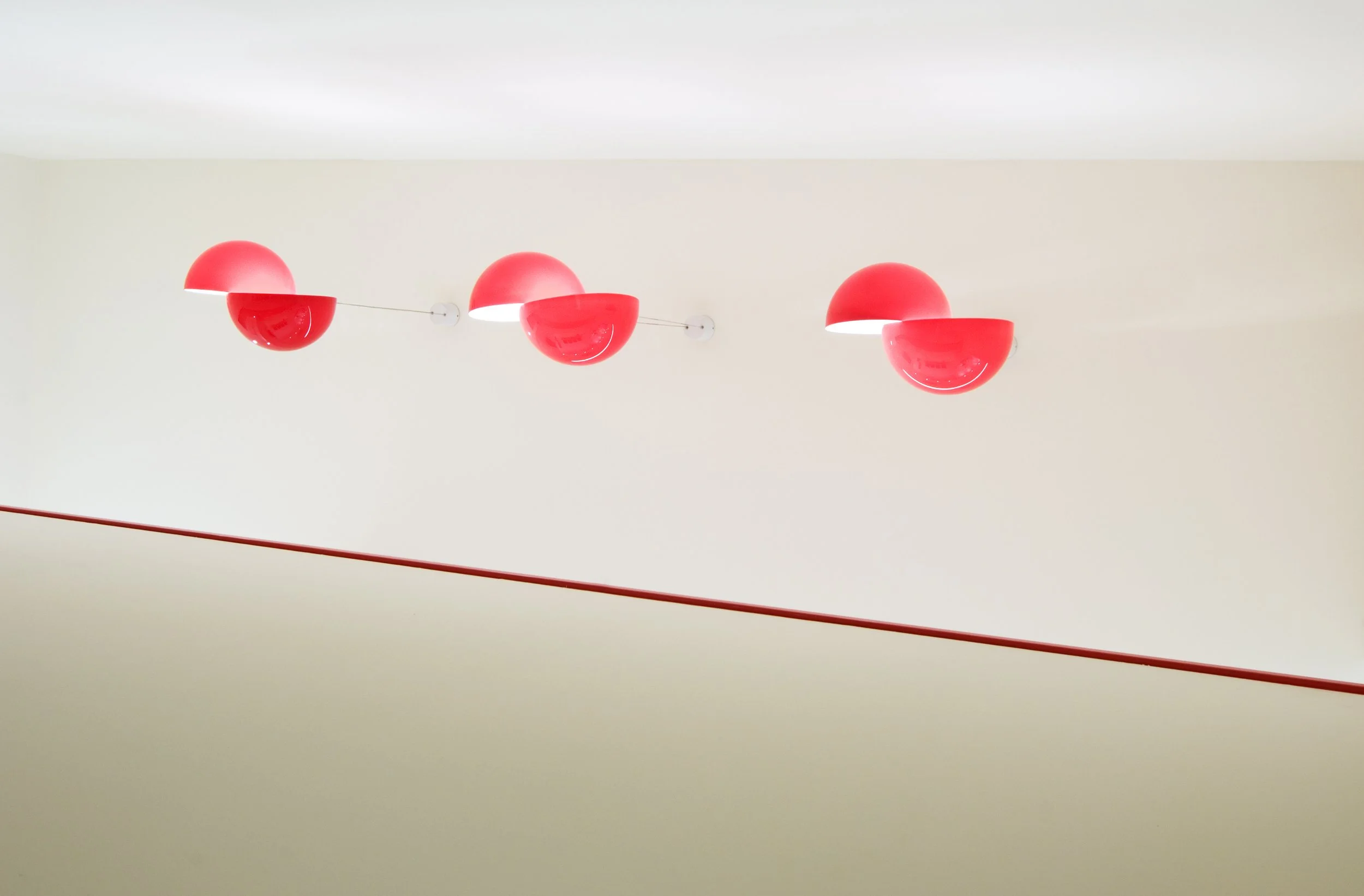 Hängende runde rote Lampen in einer Reihe an der weißen Decke, mit einer roten Linie auf der Wand darunter.