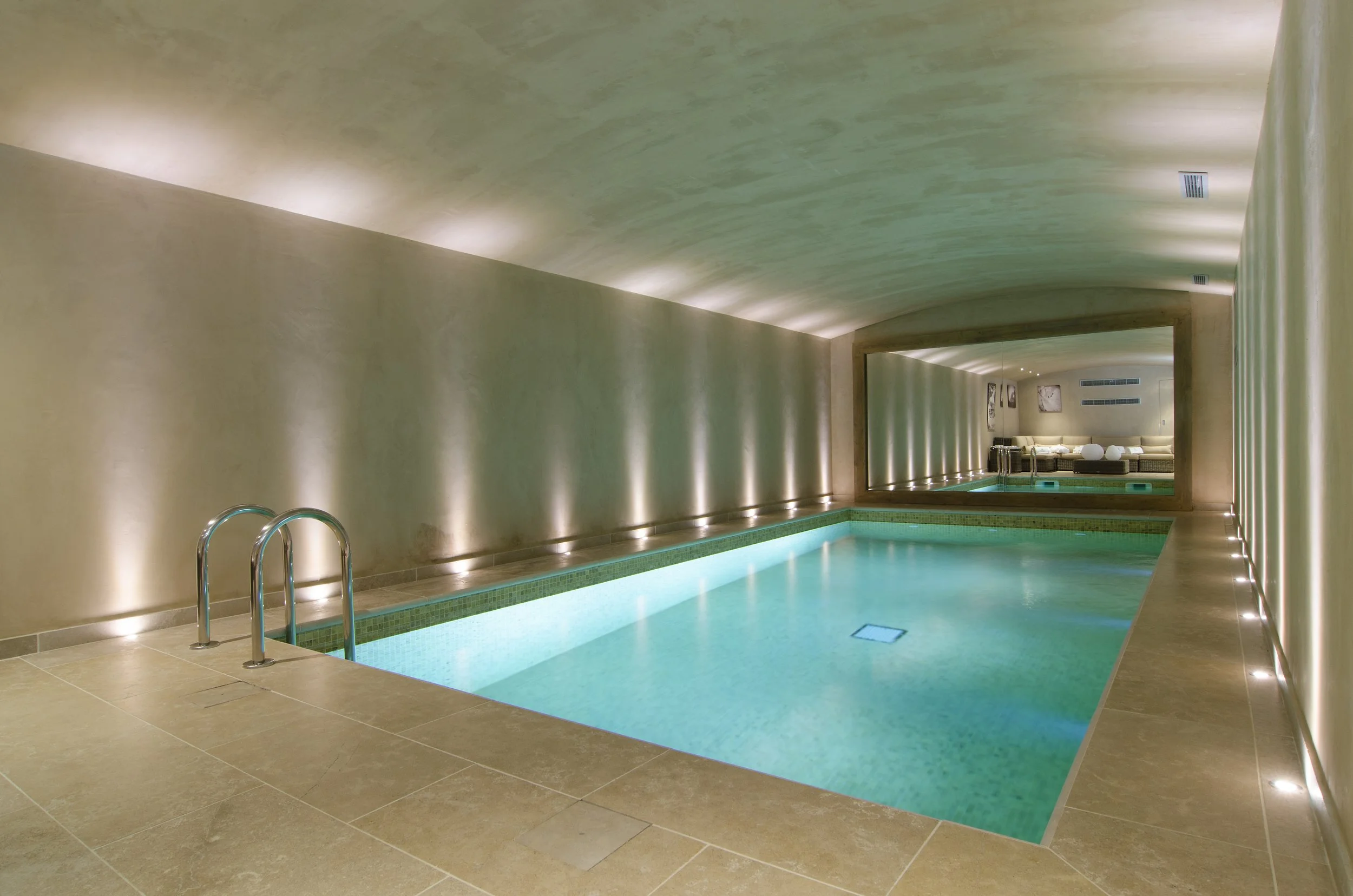 Innenaufnahme eines modernen Wellness-Bads mit kleinem beheiztem Pool, steinfarbenen Fliesen und gedämpftem, indirektem Licht.