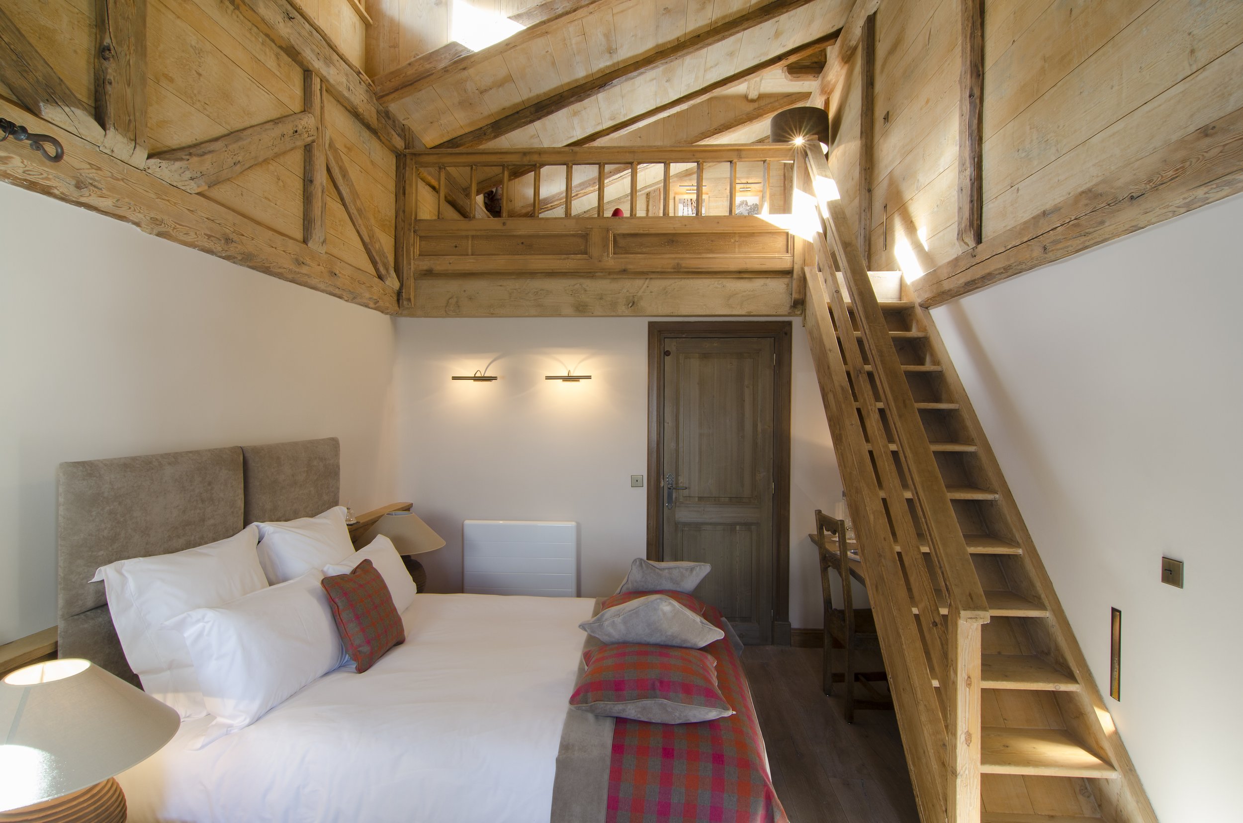 Schlafzimmer mit Doppelbett, Holzmöbeln, einer Holztreppe zur oberen Etage, und weißen Wänden.