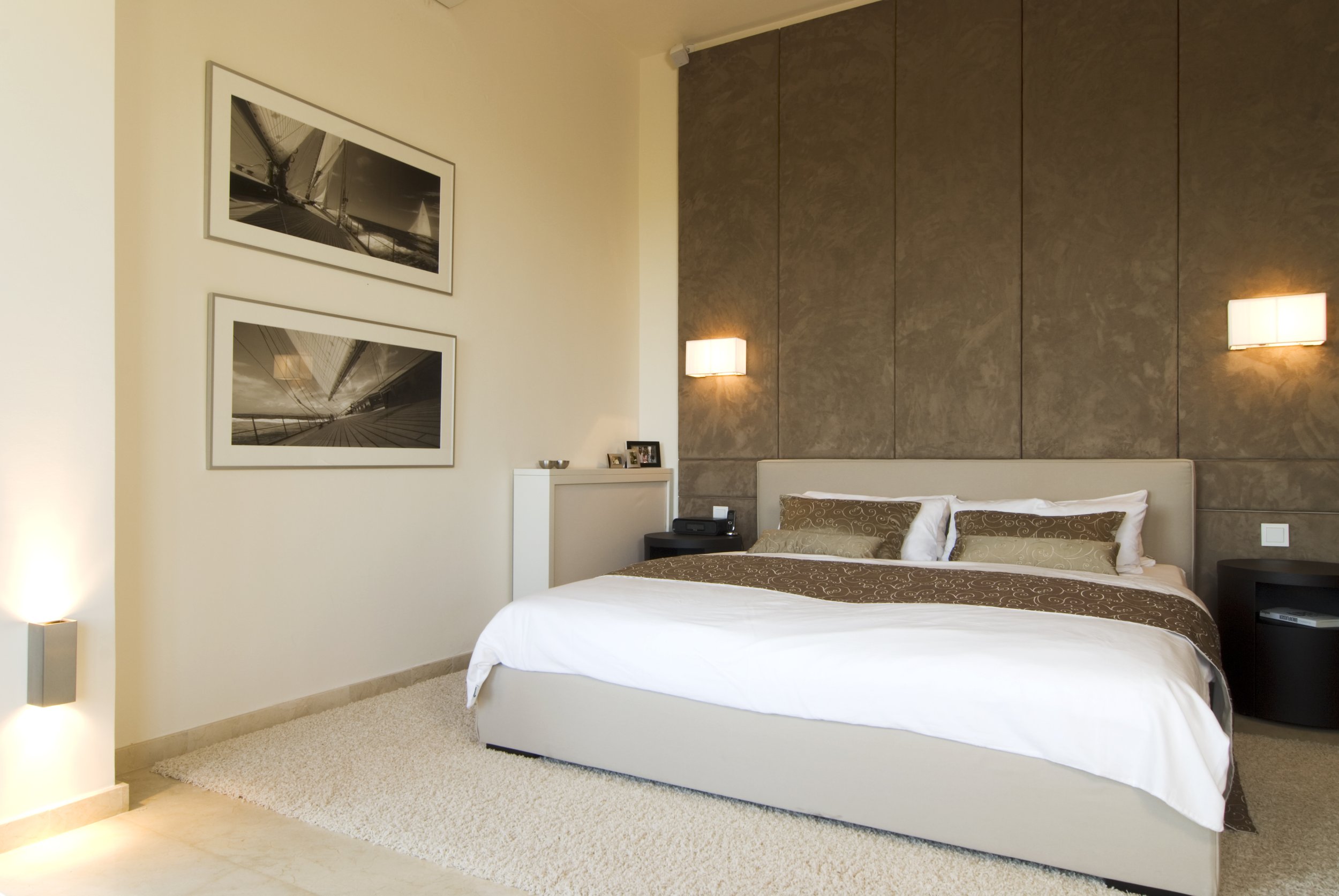 Schlafzimmer mit modernem Design, Doppelbett, Wandlampen, Kunstwerke an der Wand, Nachttische mit Dekorationsgegenständen, Teppich auf Holzboden