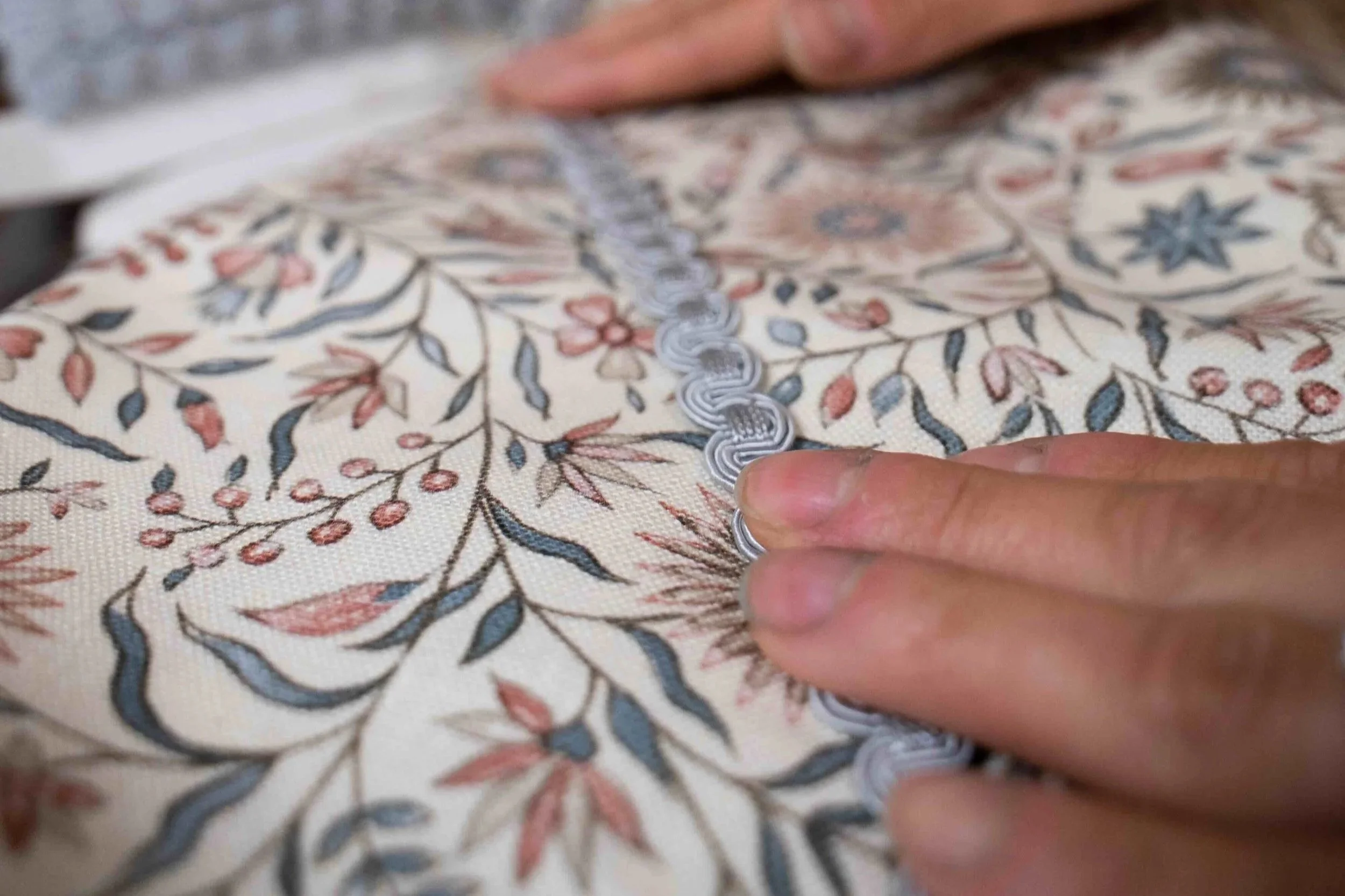 A person sewing a decorative pattern on fabric with floral and leaf designs using a crochet hook.