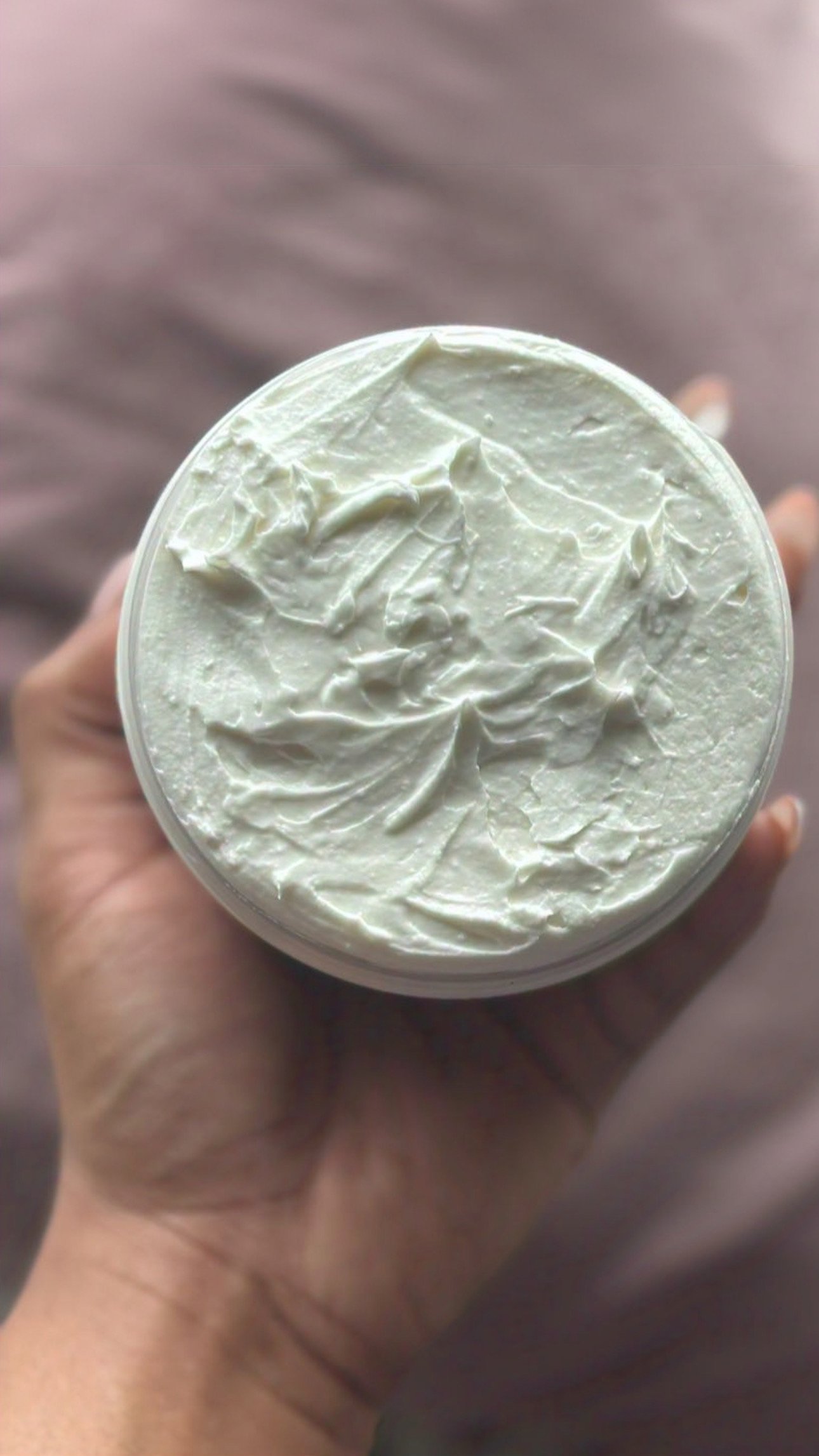 A hand holding a container of thick white cream with visible texture and swirls, against a blurred background.