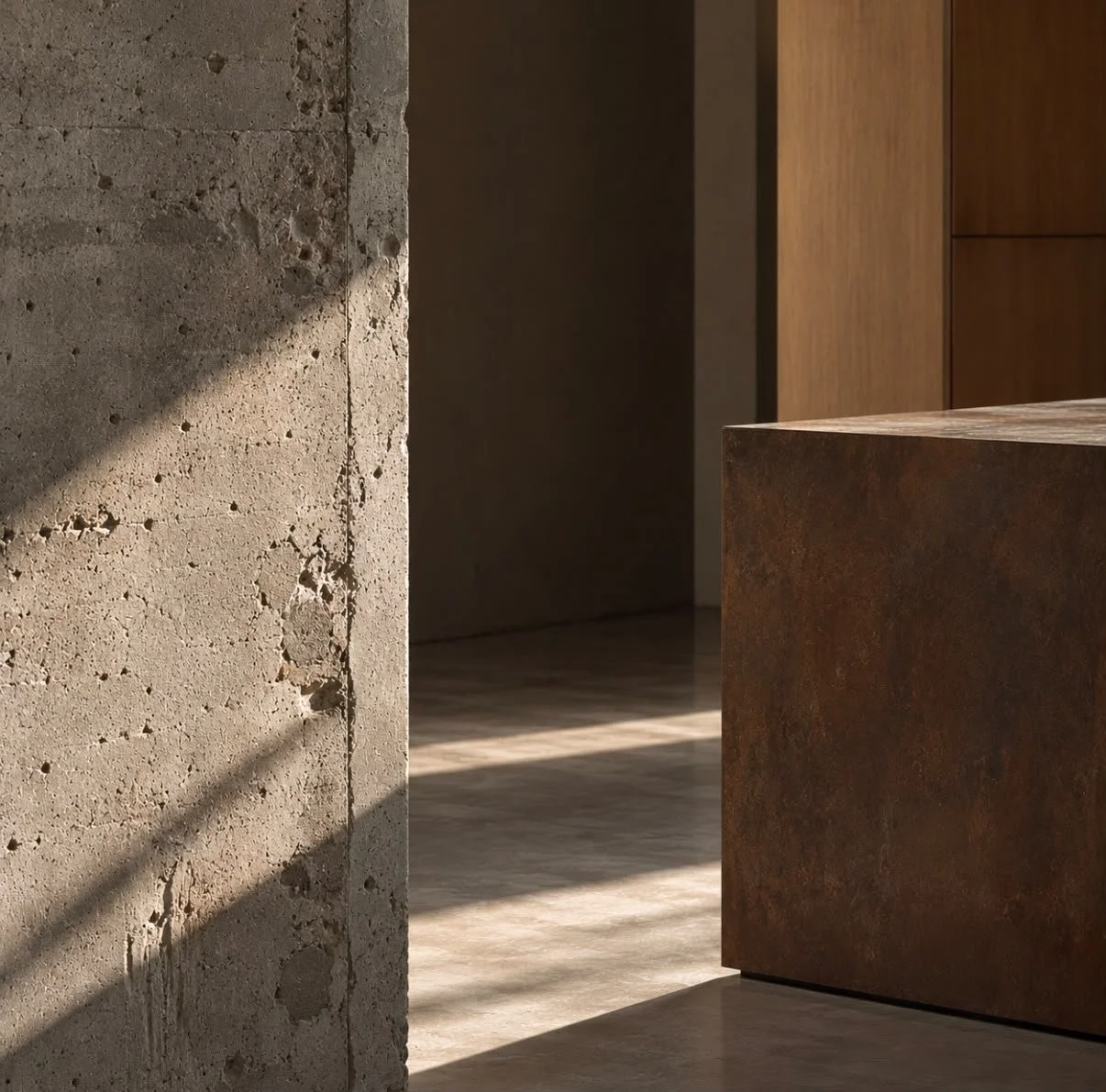 Vista de un espacio interior con pared de hormigón, solado de hormigón pulido y muebles de madera, con iluminación natural y sombras en el suelo.