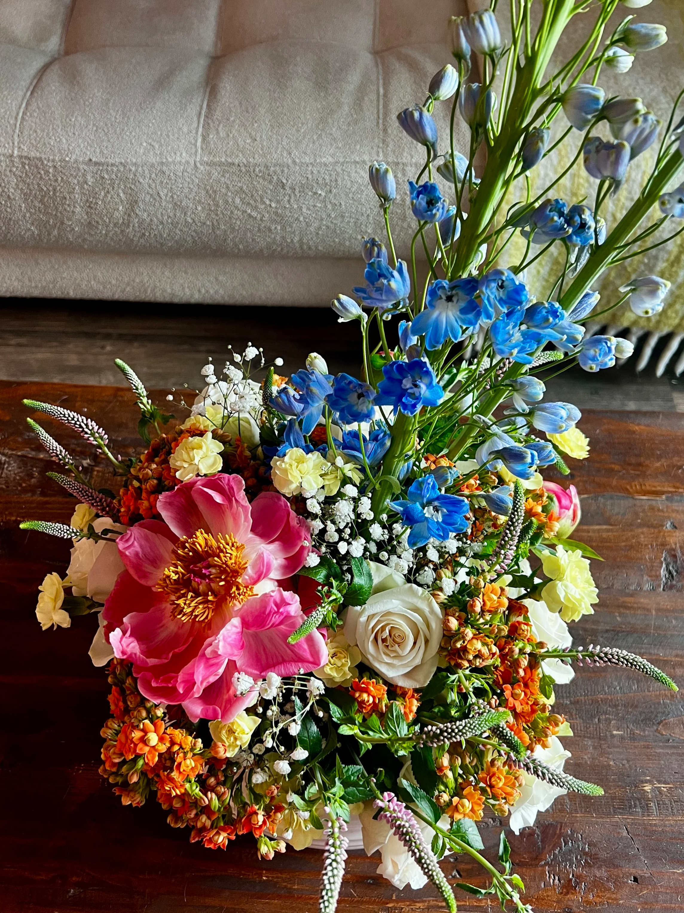 Colorful mixed flower bouquet on a wooden table with a beige couch in the background.