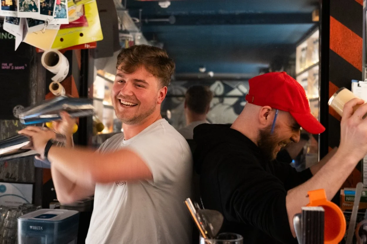 Two bartenders shaking cocktails back to back.