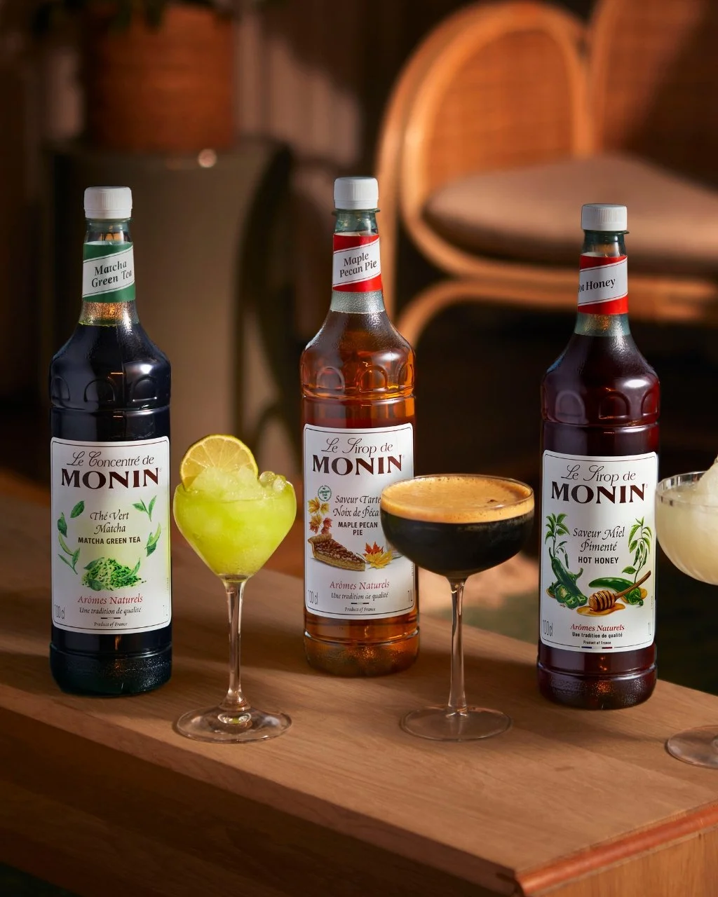 Three bottles on Monin Syrups next to three cocktails.