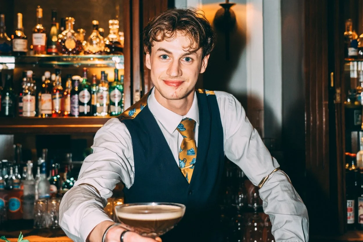 A bartender from The Grand serves a cocktail across the bar.