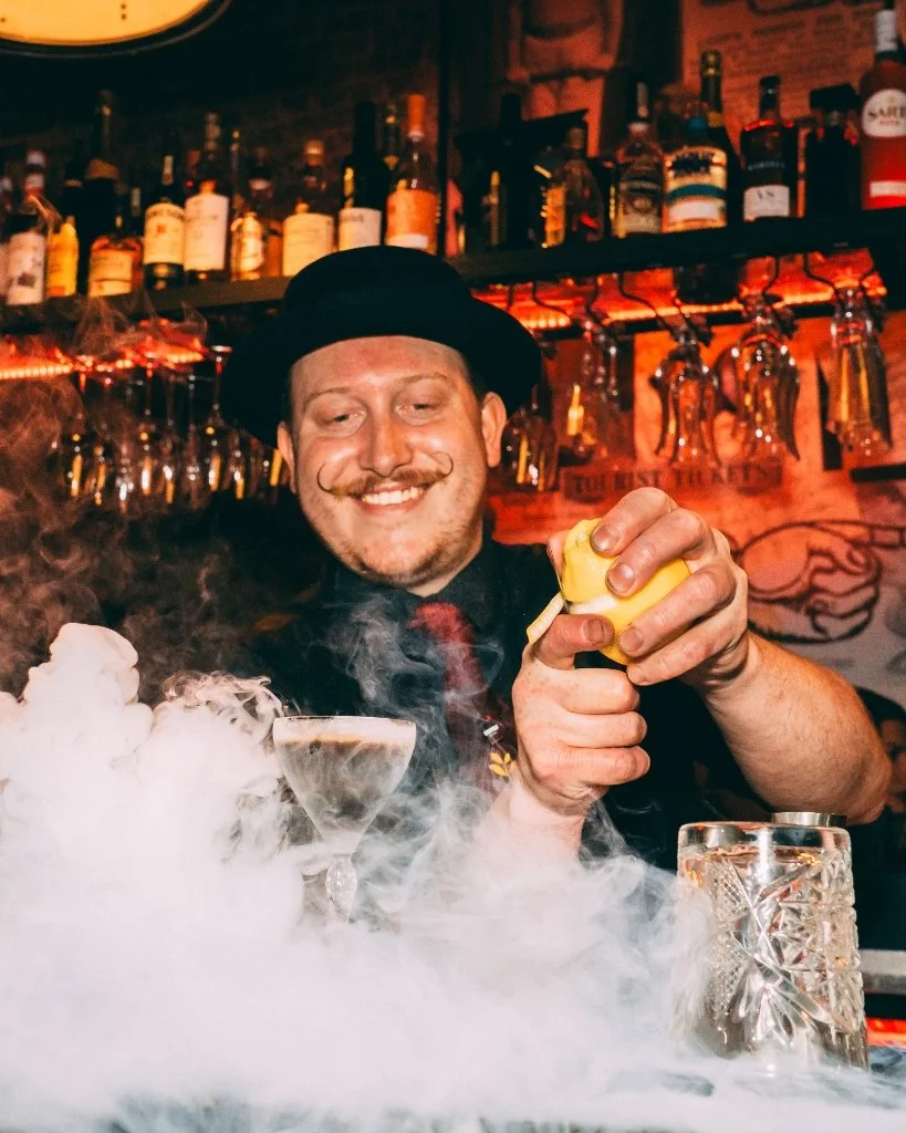 A bartender at Bohemia serving a cocktail through dry ice smoke.