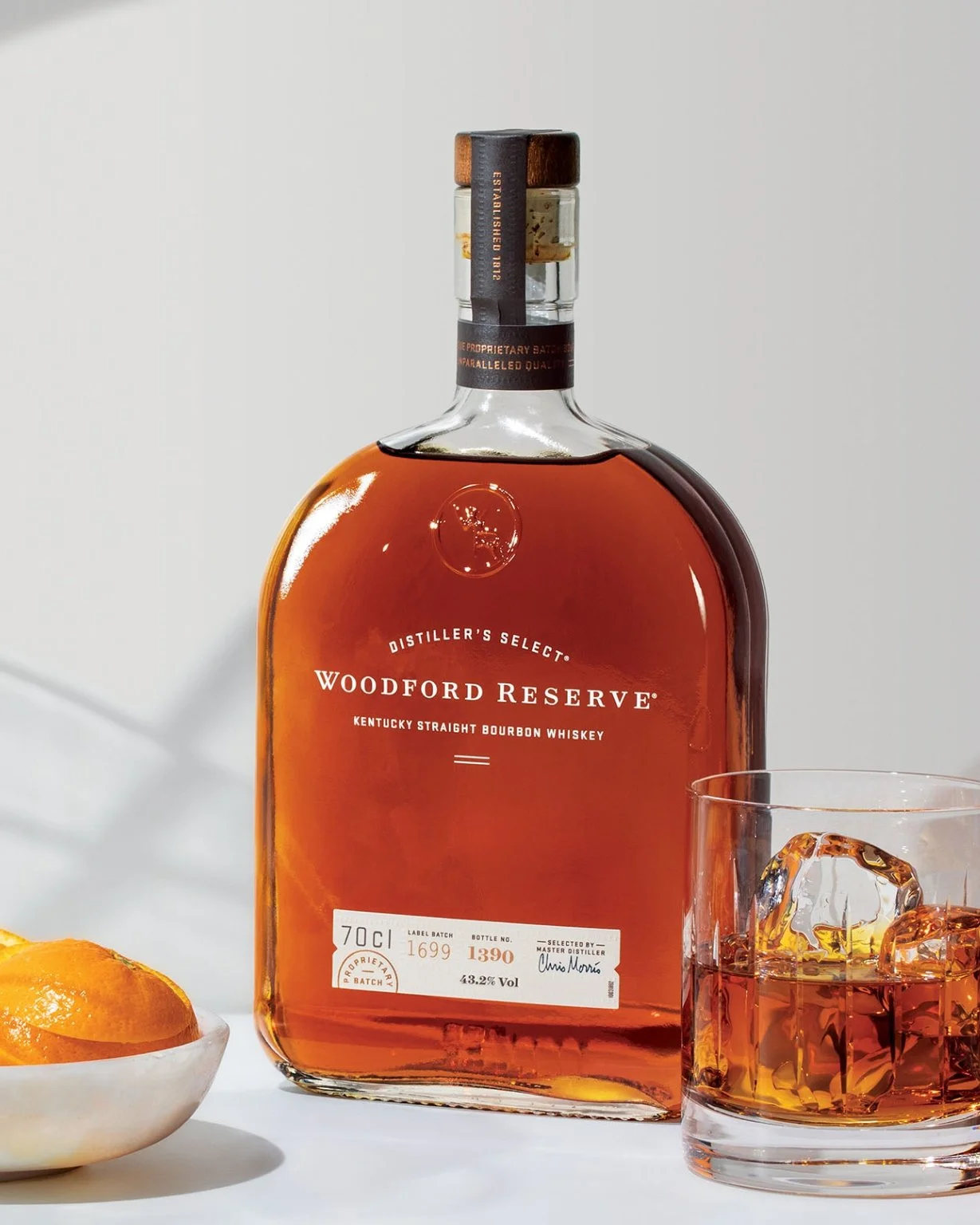 A bottle of Woodford Reserve next to a glass of whiskey and some orange slices.