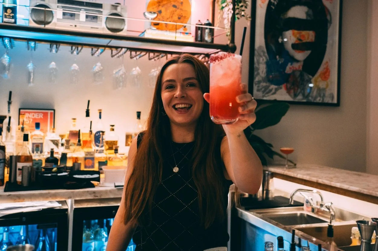 A bartender raising a cocktail to cheers.