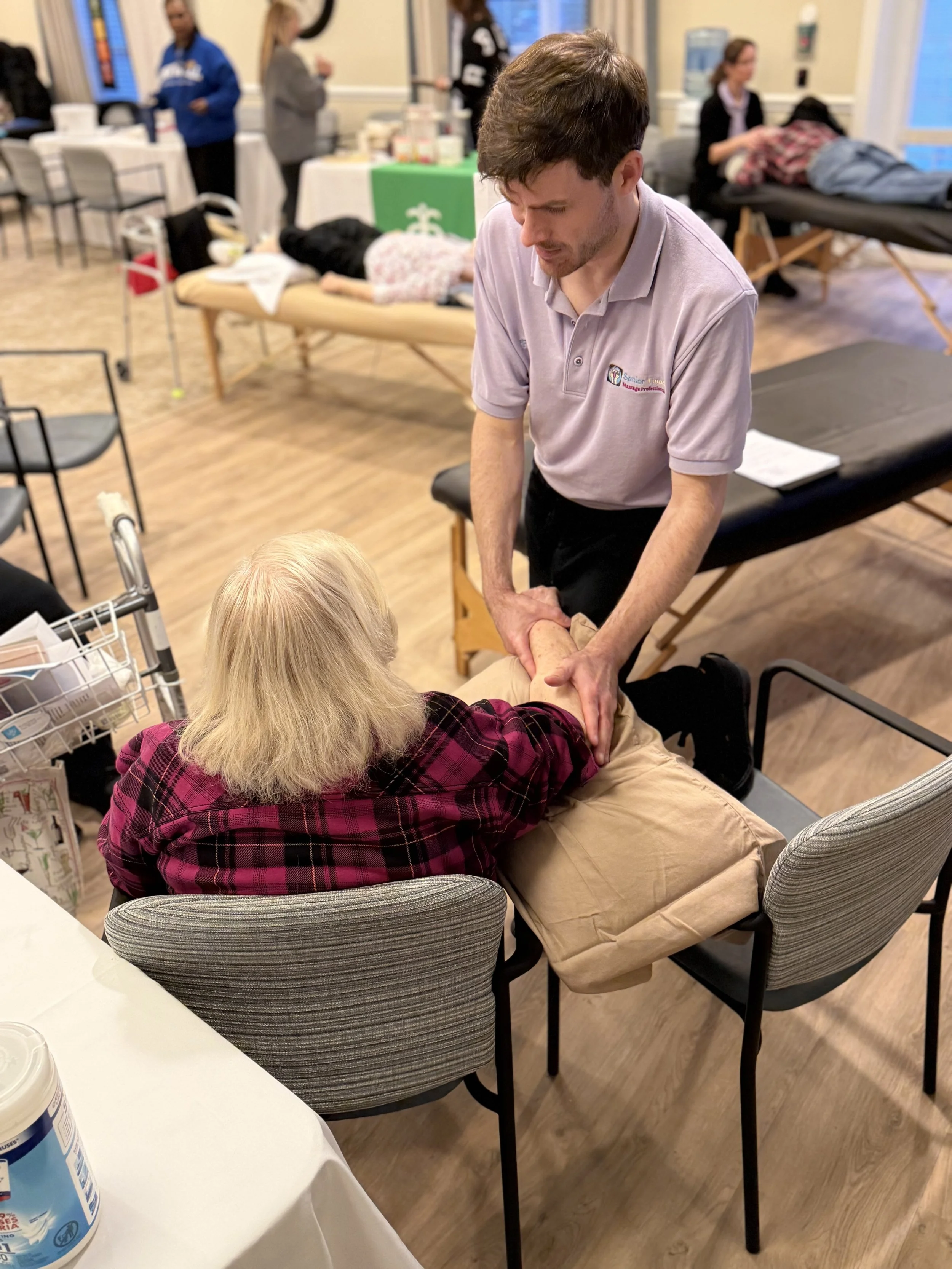 Senior Touch Massage Professionals therapist providing a gentle hand massage to an older woman during a community health and wellness event.