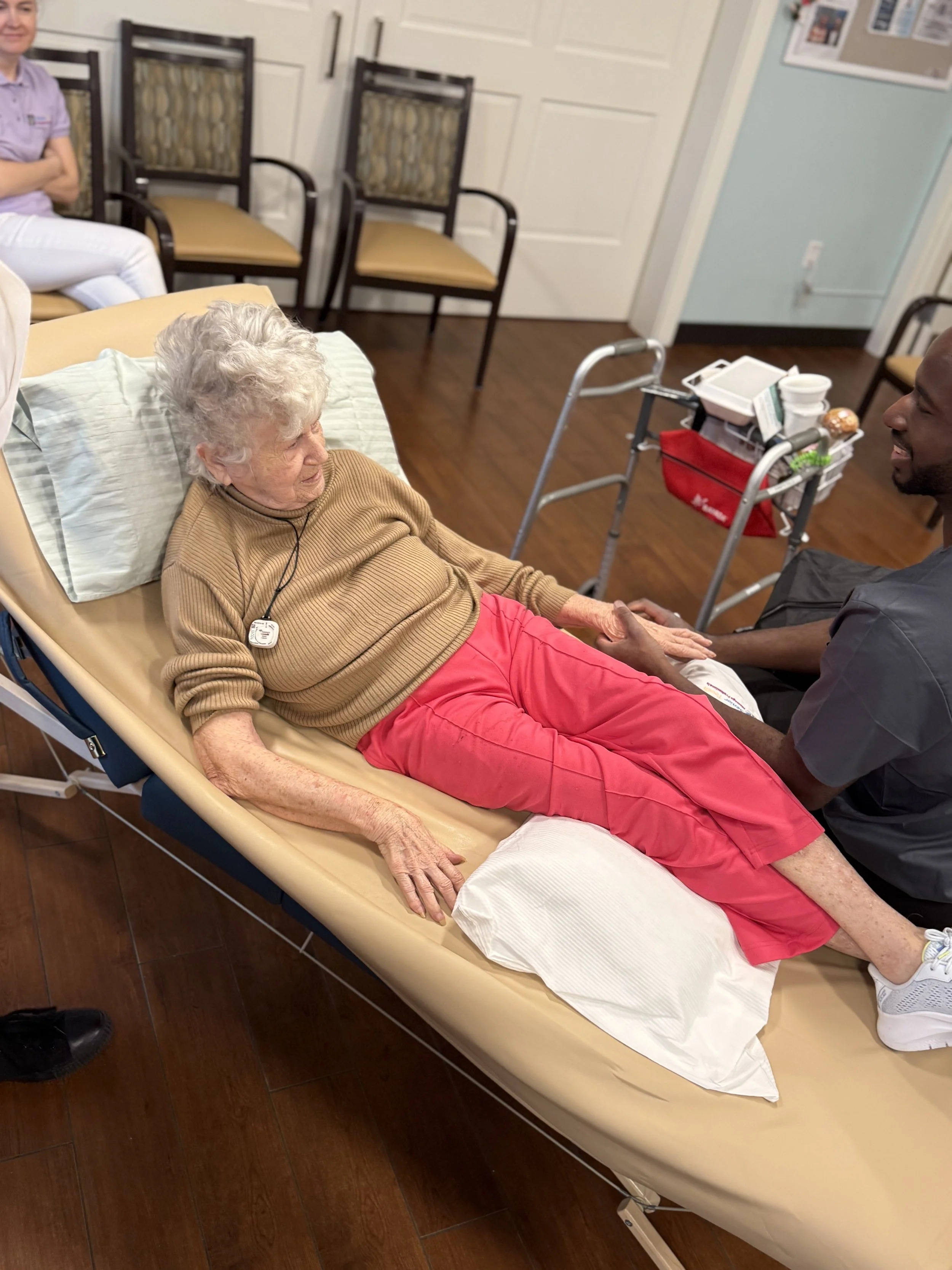 Senior Touch Massage Professionals therapist holding hands with an older woman resting in bed, providing compassionate bedside comfort and personalized attention.