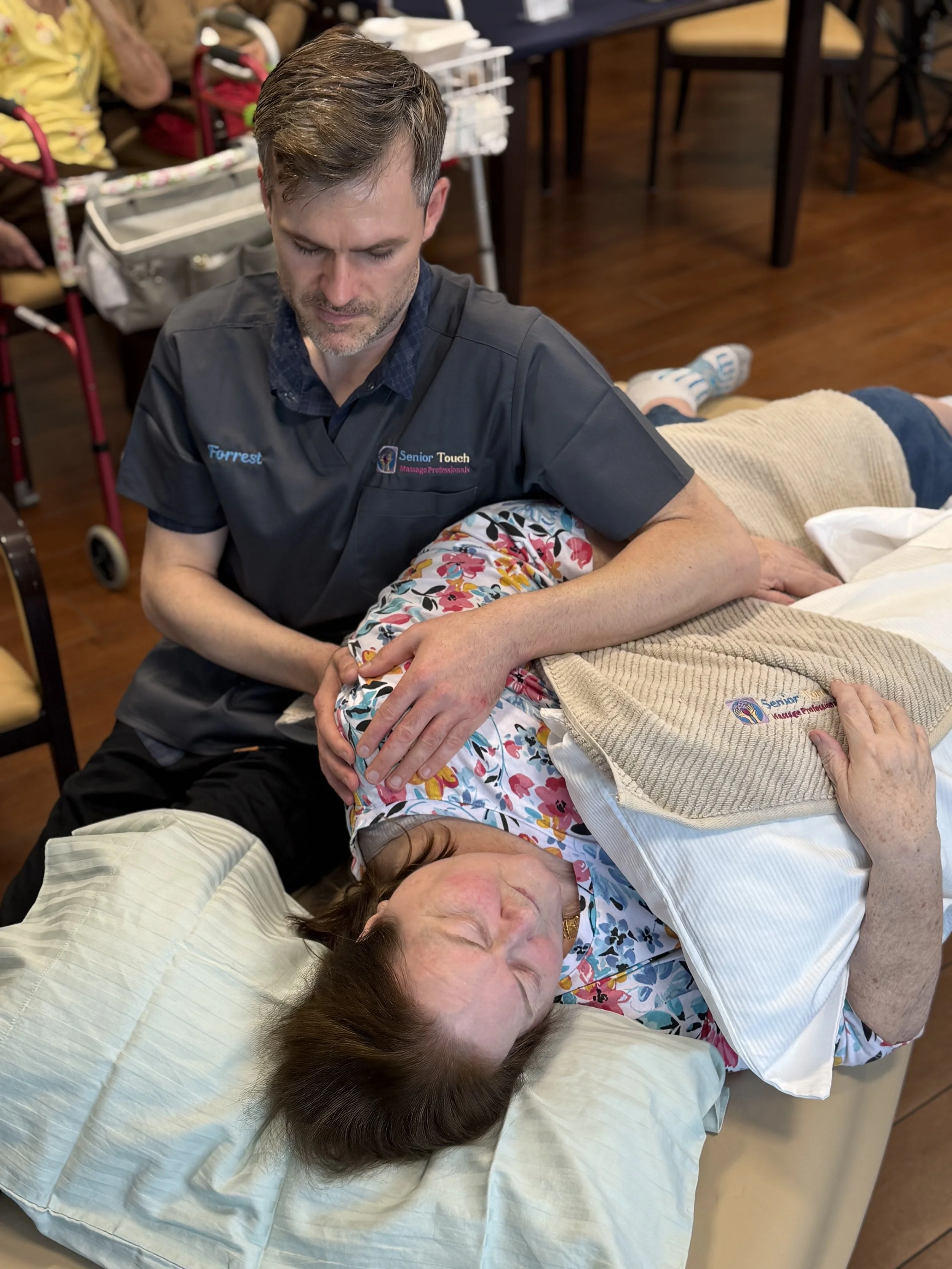 Senior Touch Massage Professionals therapist providing therapeutic massage to an older woman resting comfortably on a massage table during a group wellness session.