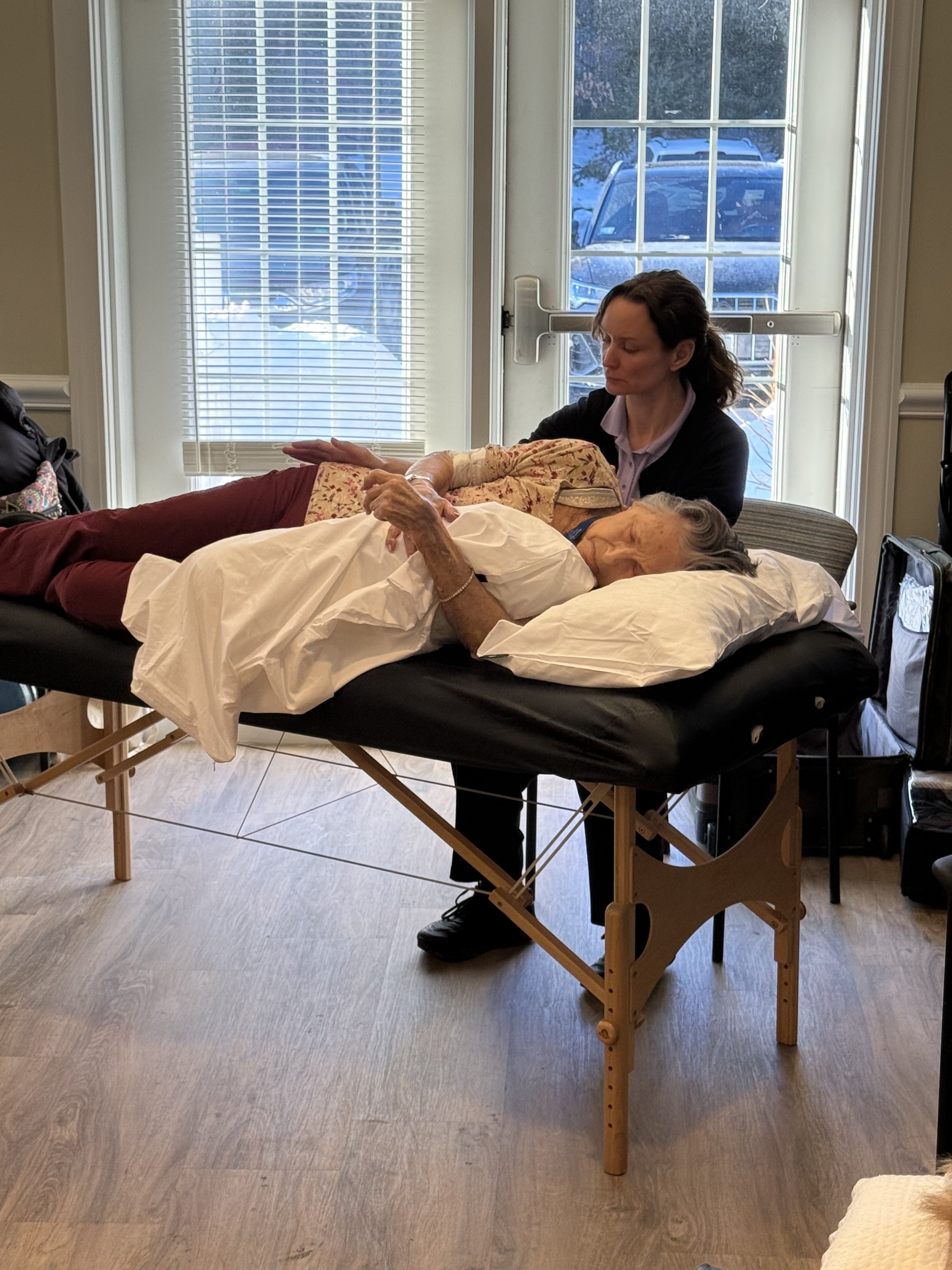 Senior Touch Massage Professionals therapist providing a gentle therapeutic massage to an older woman resting on a treatment table indoors.