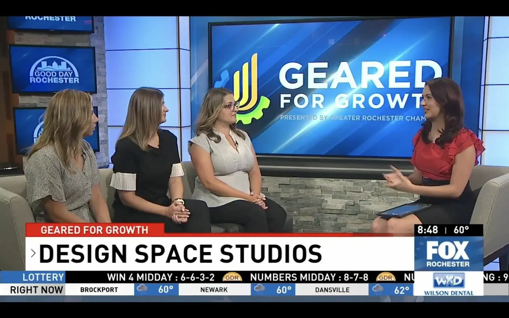 Television shows a news interview on 'Good Day Rochester' about design space studios, with four women seated in a studio and a female interviewer talking. The background features the show's logo and graphics about growth.