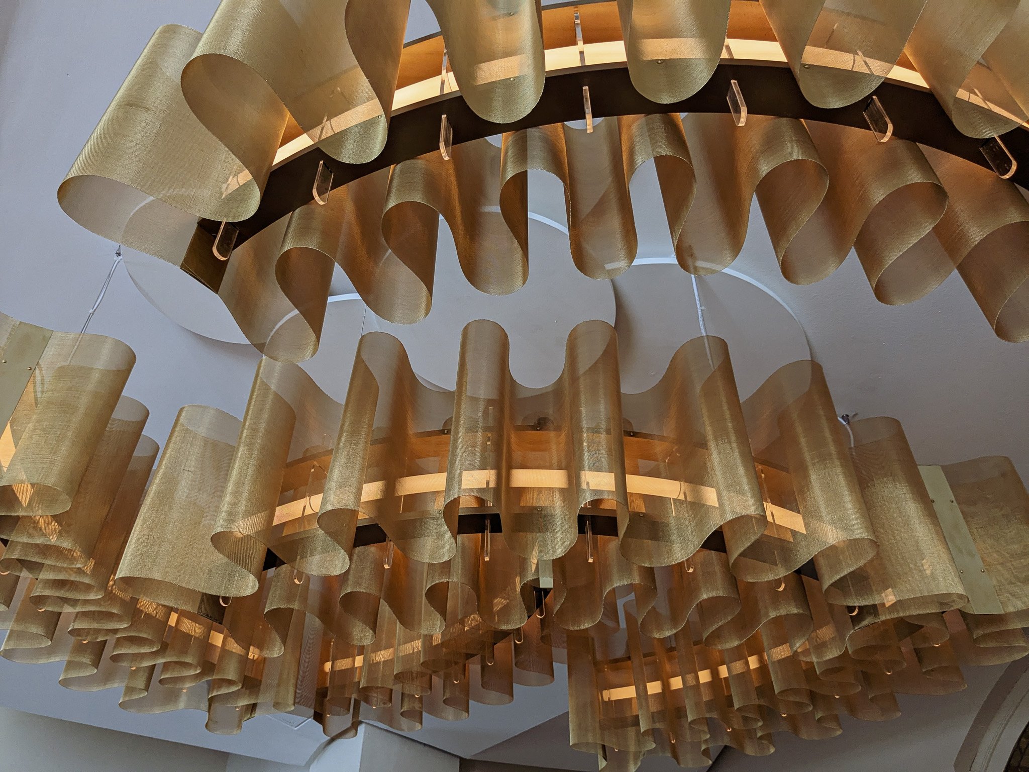 A large decorative chandelier with multiple layers of gold-colored fabric or metal loops hanging from a central fixture.