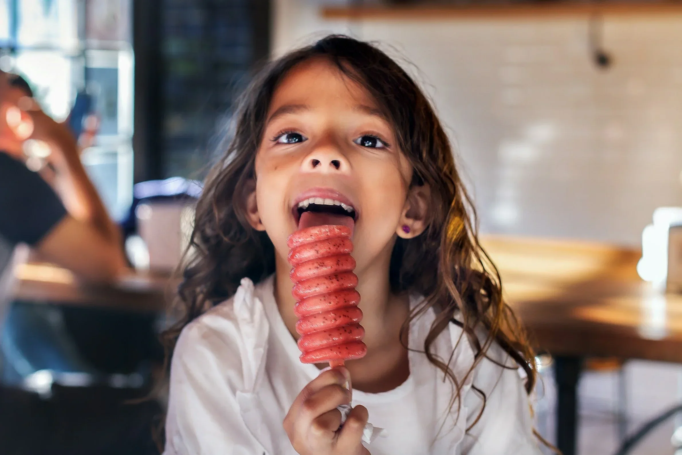 Mädchen  isst ein rotes, spiralförmiges Eis am Stiel