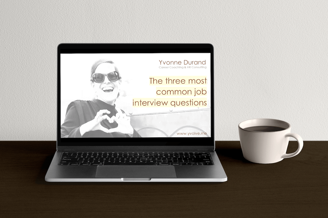 Laptop on a wooden desk displaying a slide with the title 'The three most common job interview questions'