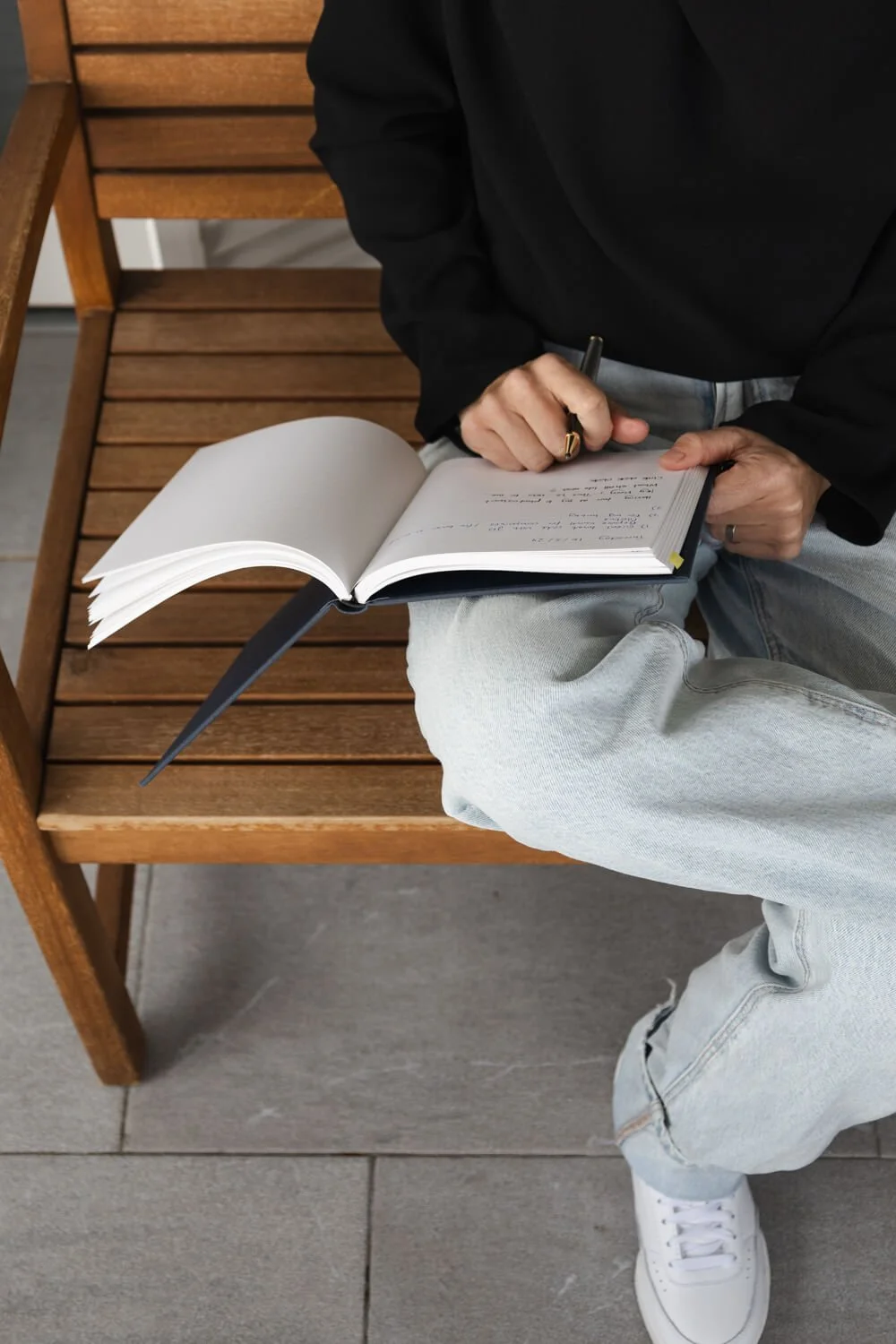 Close-up of Yvonne’s hand writing in a notebook while sitting on a wooden bench