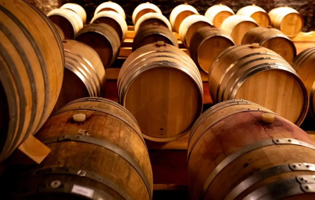 Multiple wooden barrels stored in a cellar or warehouse for wine or spirits aging.