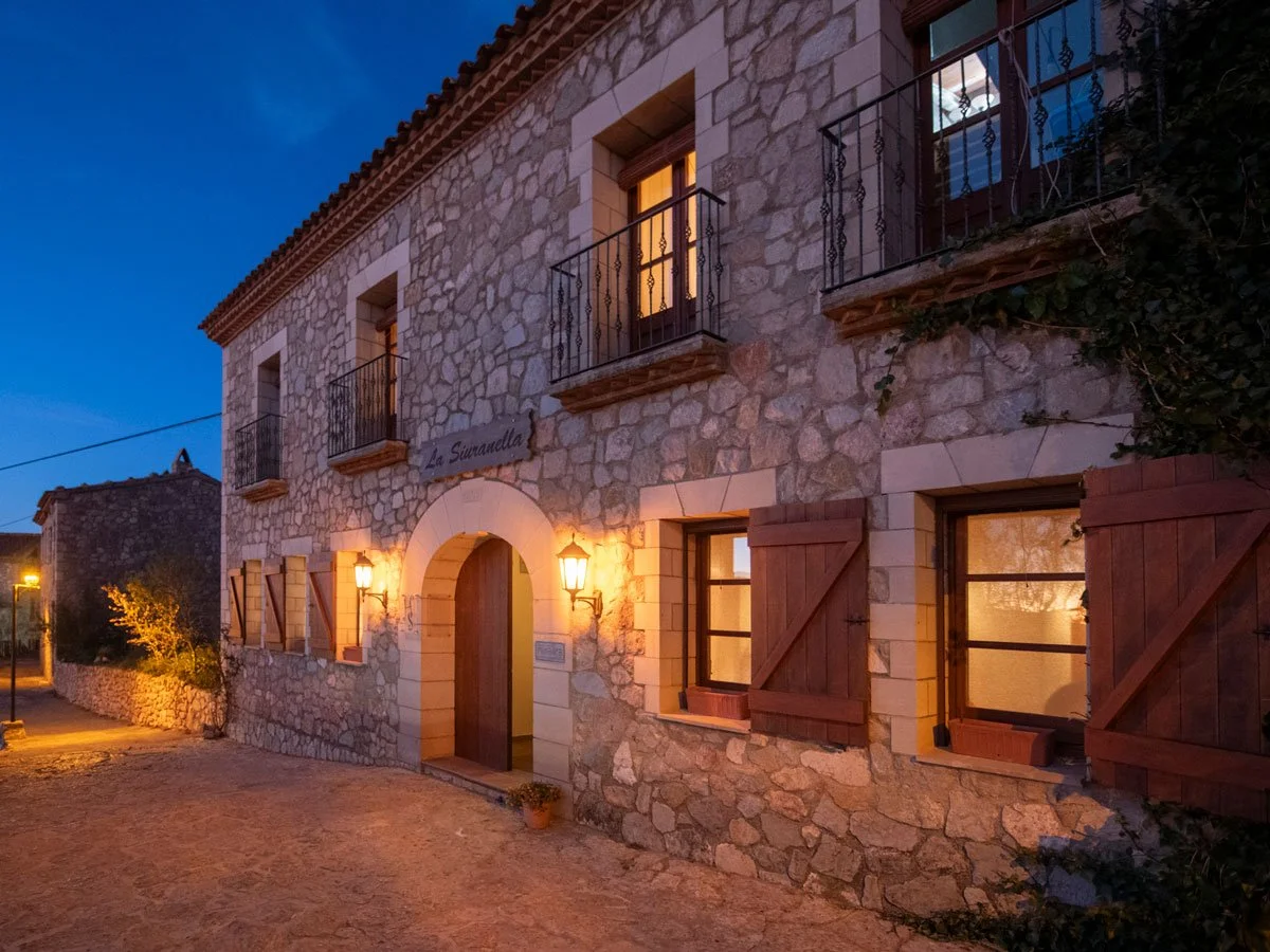 Stone building with wooden shutters, balconies, and warm lights at dusk.