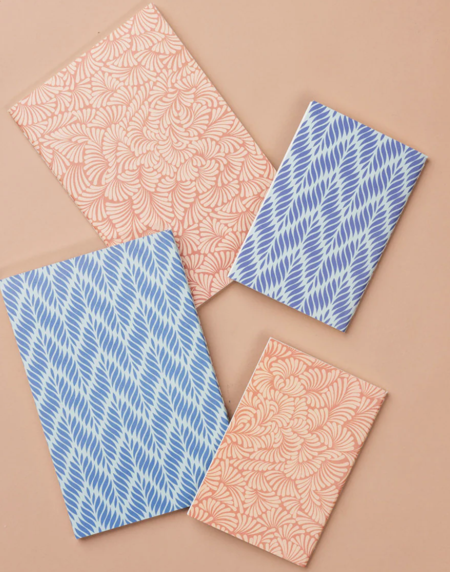 Patterned notebooks with pink and blue leaf designs on a peach-colored background.