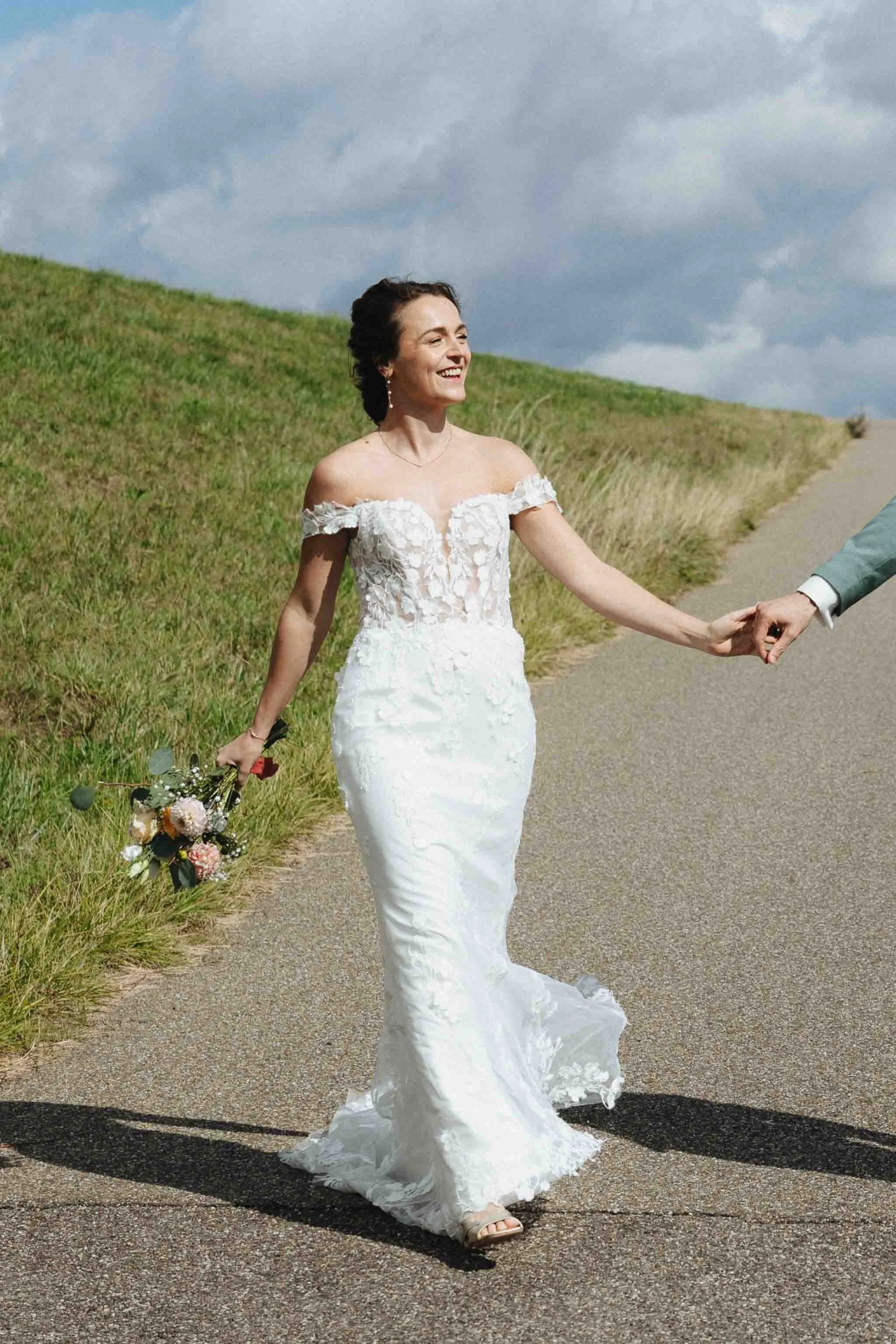 bruid loopt hand in hand met bruidegom langs de waal in nijmegen in de zon en lacht