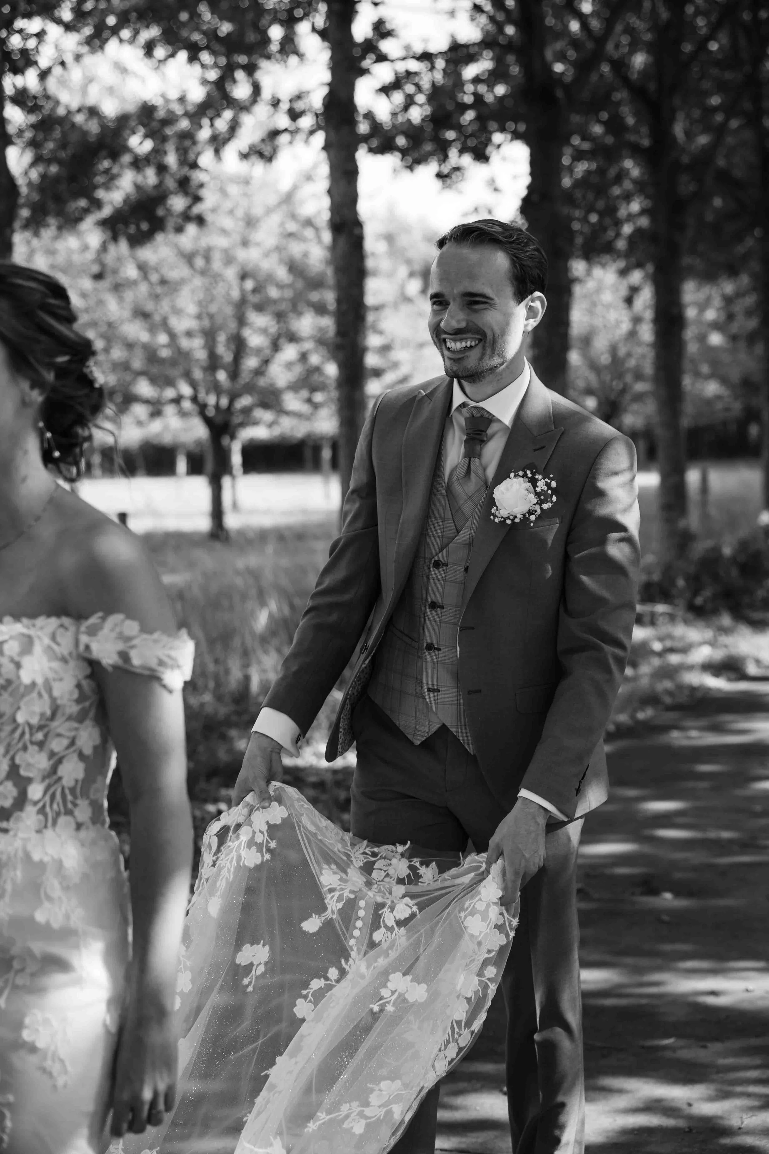 bruidegom draagt de sleep van de bruidsjurk en lacht 