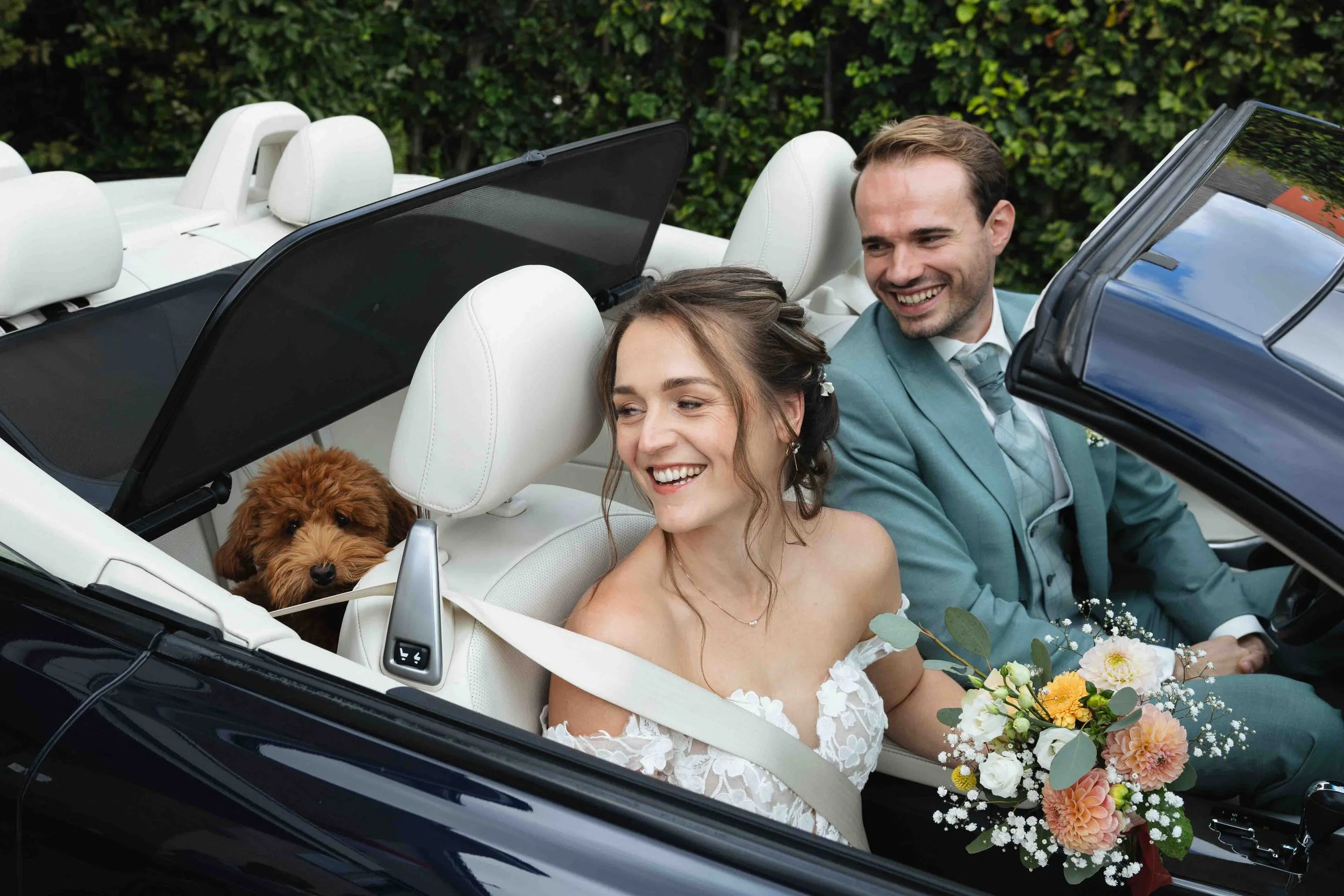 bruidspaar in cabrio met een hondje achterin de auto