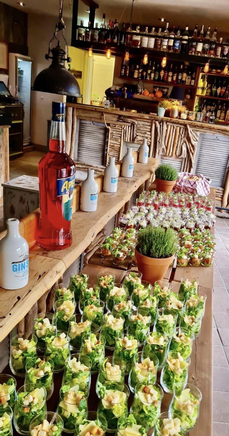 Getränkeflaschen und Salate in Gläsern auf einem Tisch arrangiert, Bar im Hintergrund.