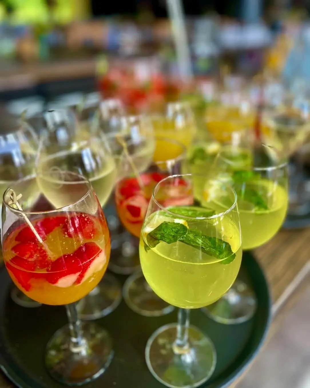 Verschiedene bunte Cocktails in Weingläsern, garniert mit Früchten und Kräutern, auf einem Tablett.