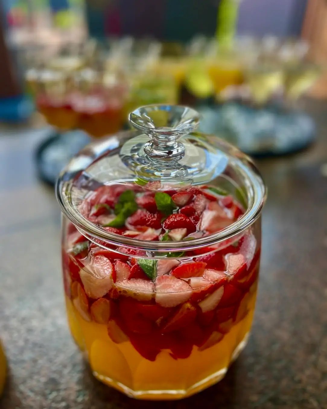 Glasbehälter mit gelber und roter Flüssigkeit, dekoriert mit Fruchtstücken und Minzblättern.