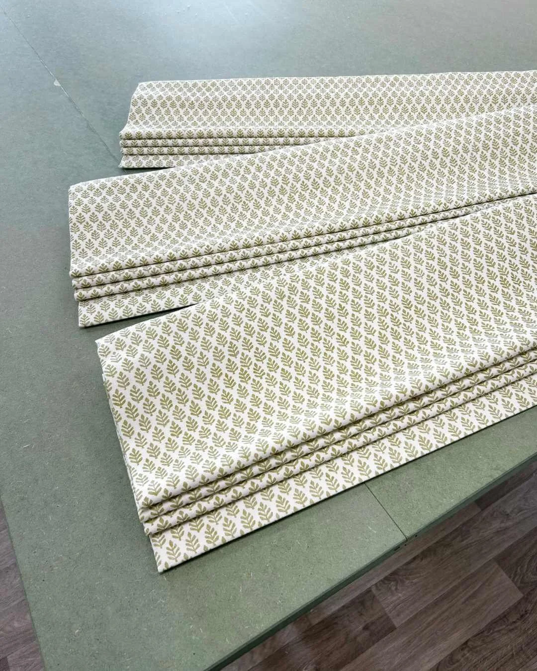 Three handmade bespoke roman blinds fully folded on the Aconite Interiors green work bench